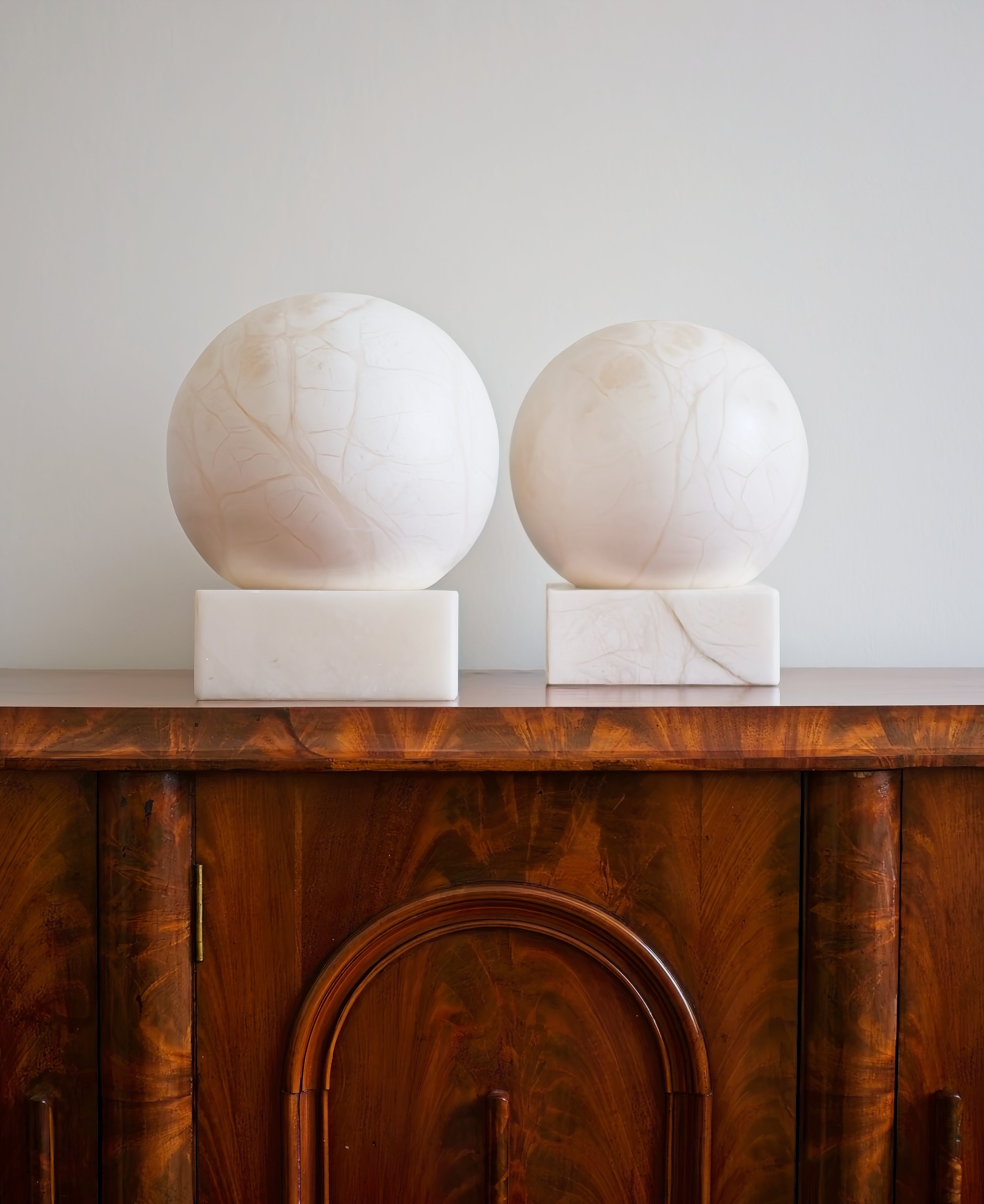 Two spherical white marble sculptures on a wooden cabinet against a cream wall.