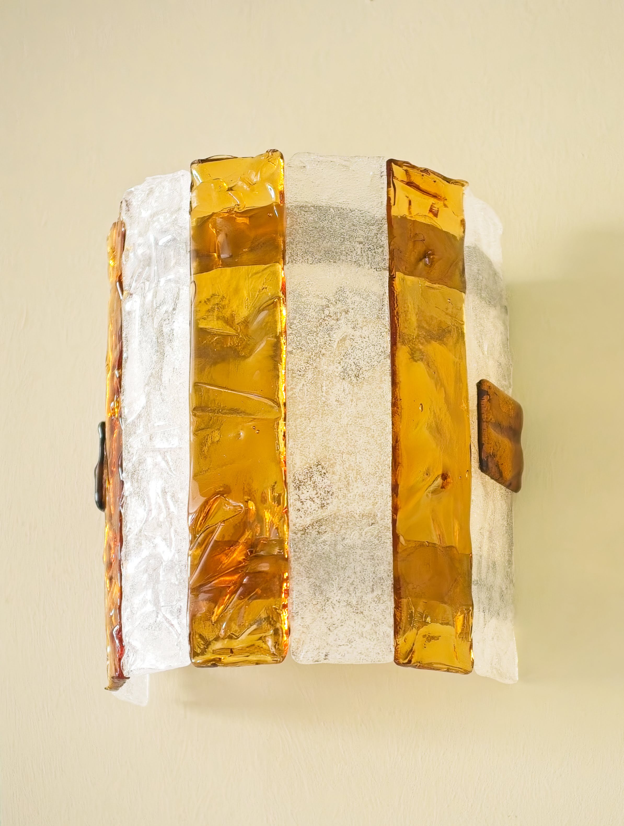 A light olive room with a brown vintage wood table and chairs with a small red marble An amber and white striped 1970s mid century modern Murano glass wall sconce by Carlo Nason For Mazzega hanging on a olive coloured wall.
