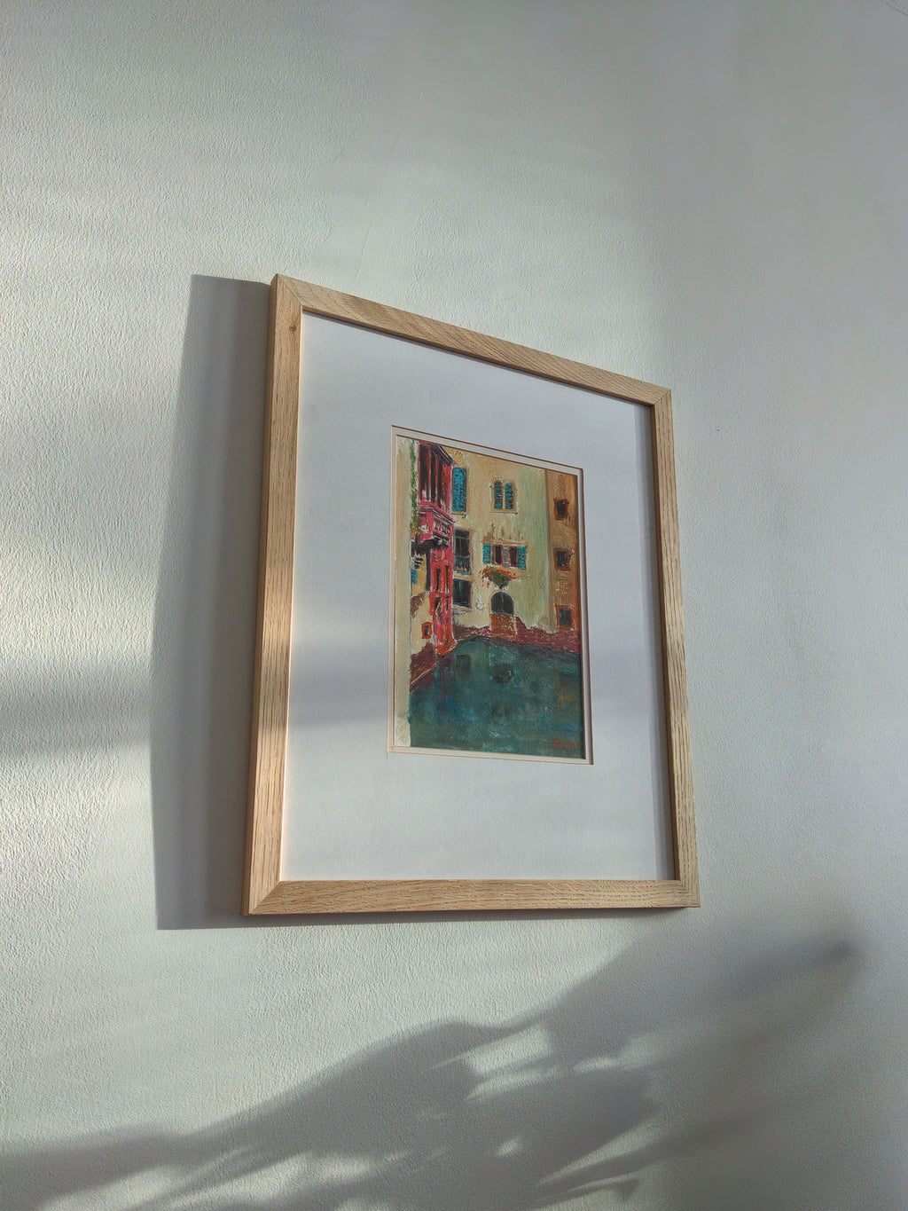 A pine framed original 1980s multi-coloured watercolour painting of a Venetian canal scene on a white wall.