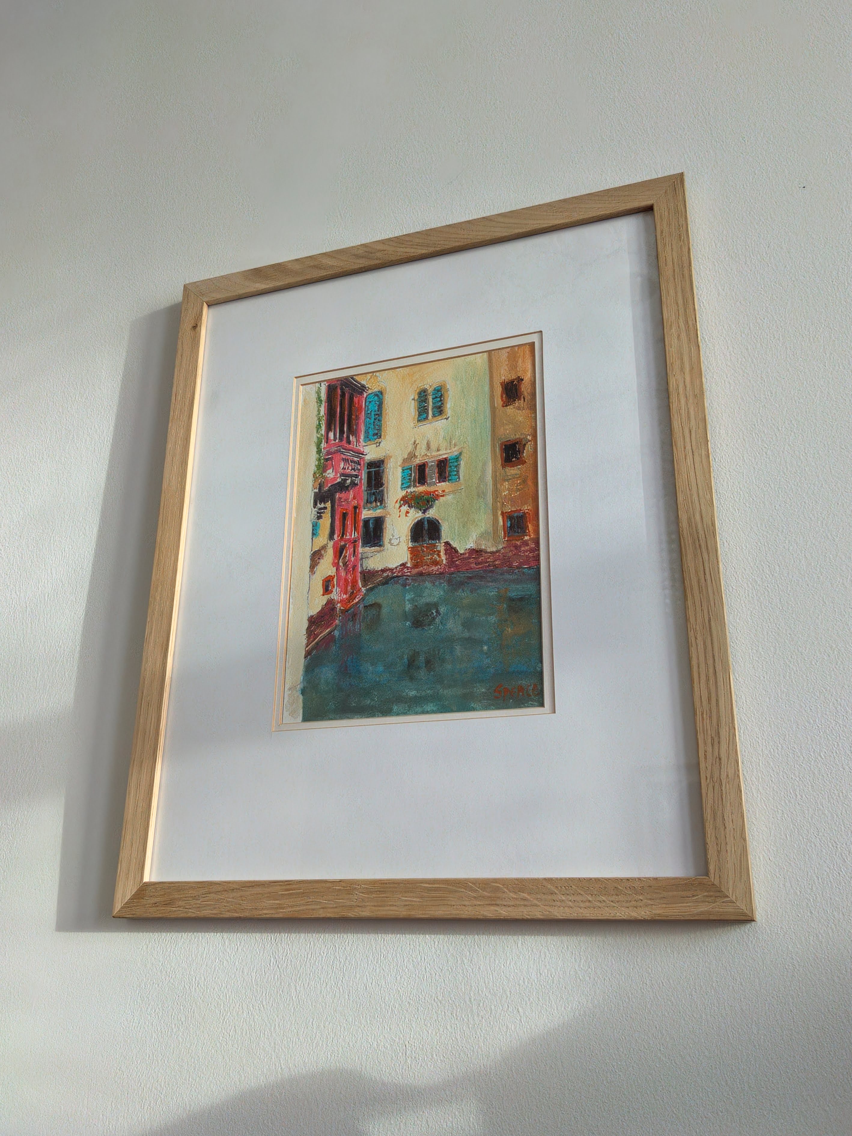 A pretty framed original vintage watercolour painting of a Venice canal scene on a white wall from below.