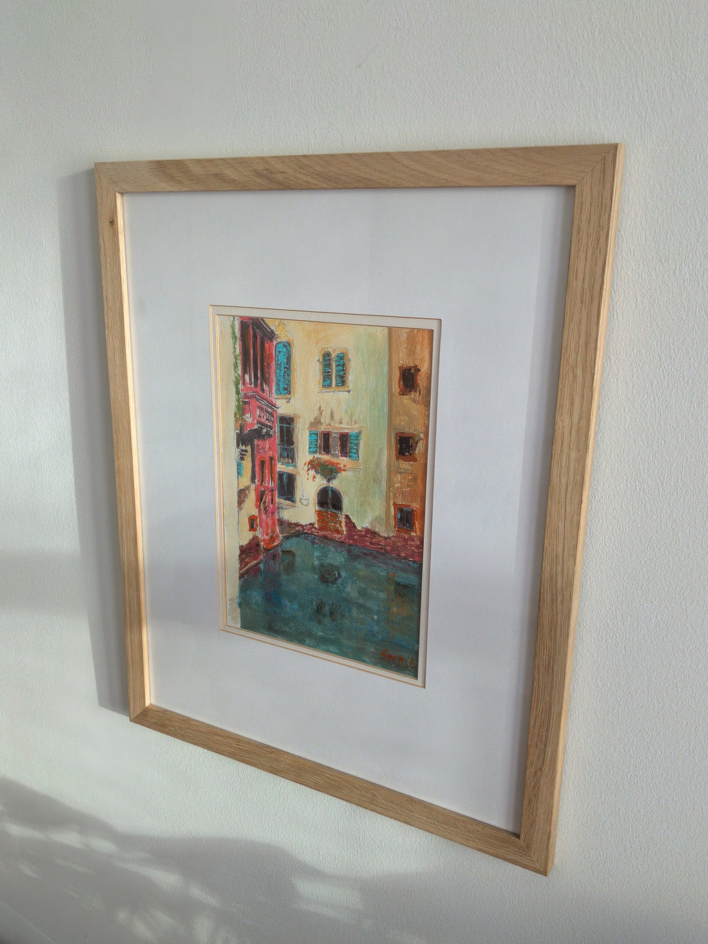 A close up of a pine framed original vintage watercolour painting of a brightly coloured Venice canal scene on a white wall by Scottish artist P.H. Spence.