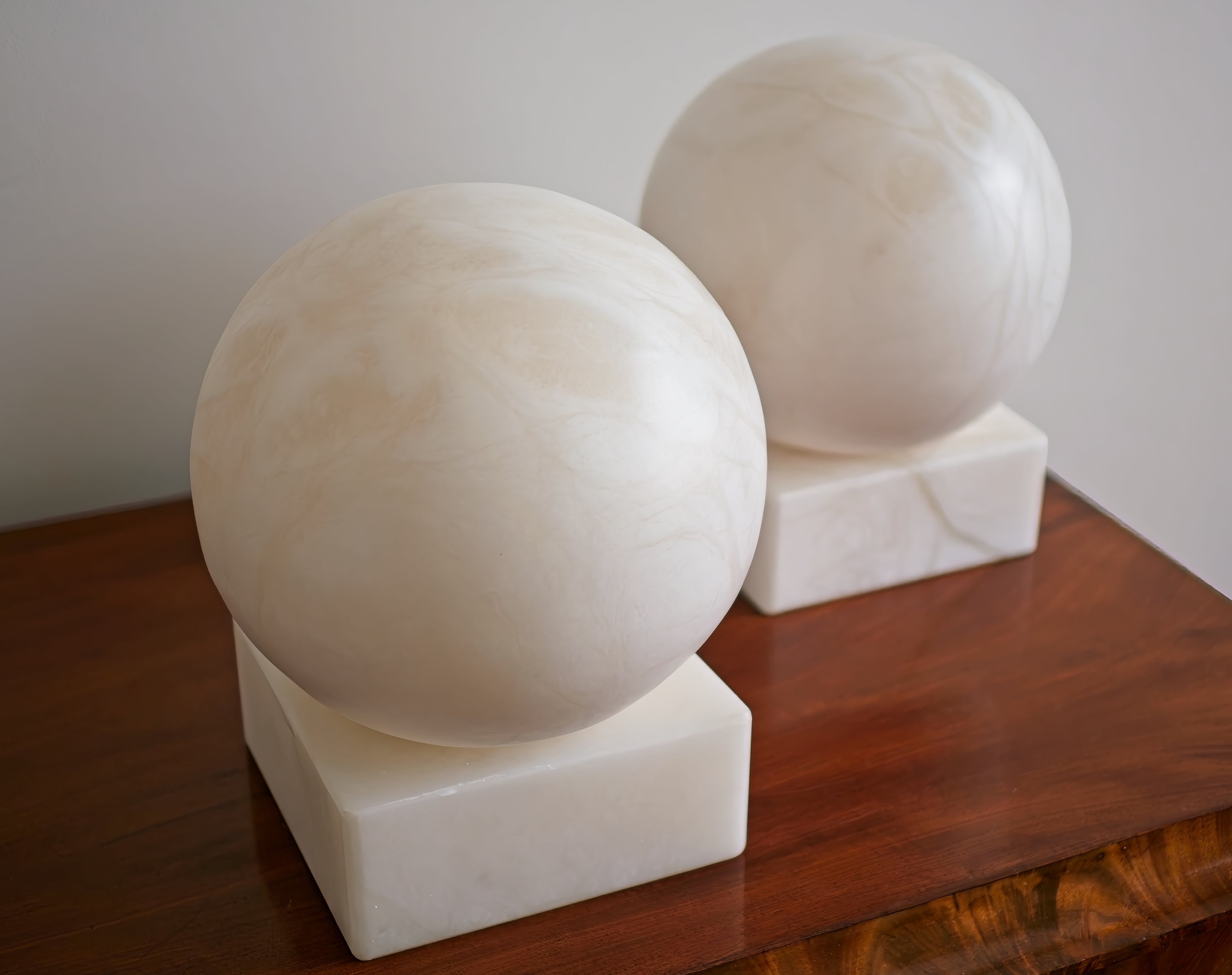 Two white marble spheres on a wooden surface with a plain background.