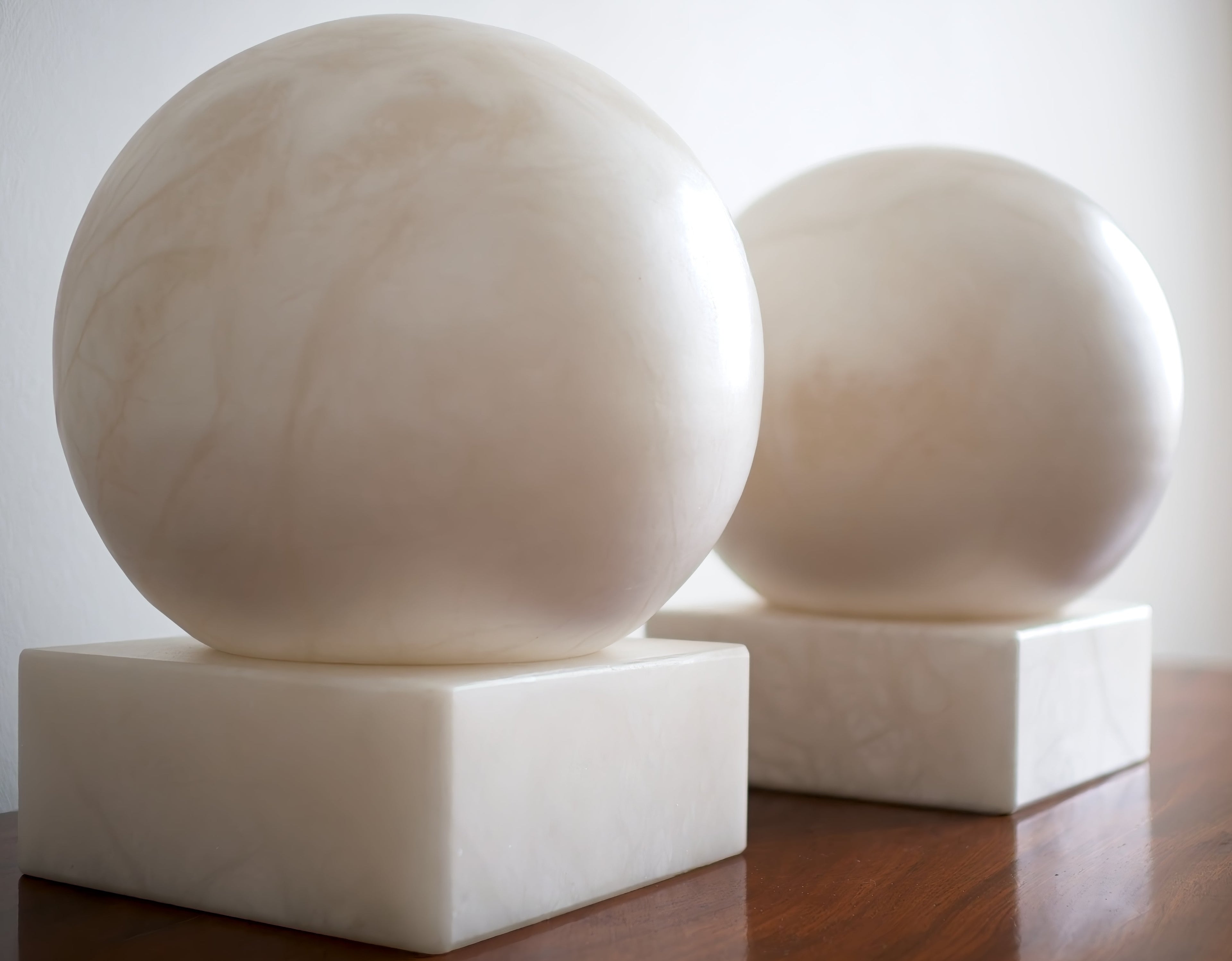 Two white marble spheres on square bases against a white background.