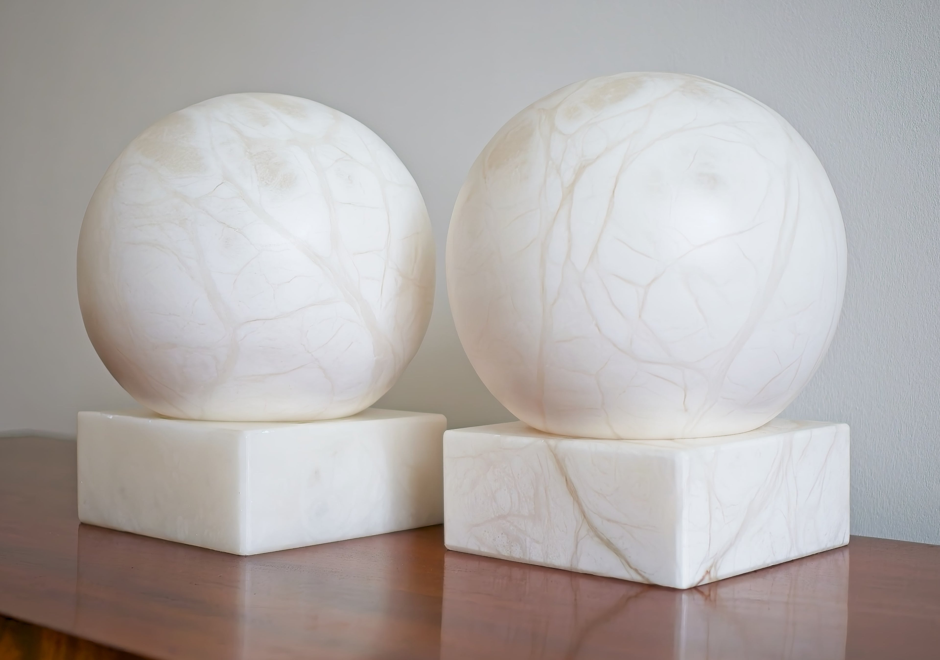 Two spherical marble lamps on square bases against a plain background