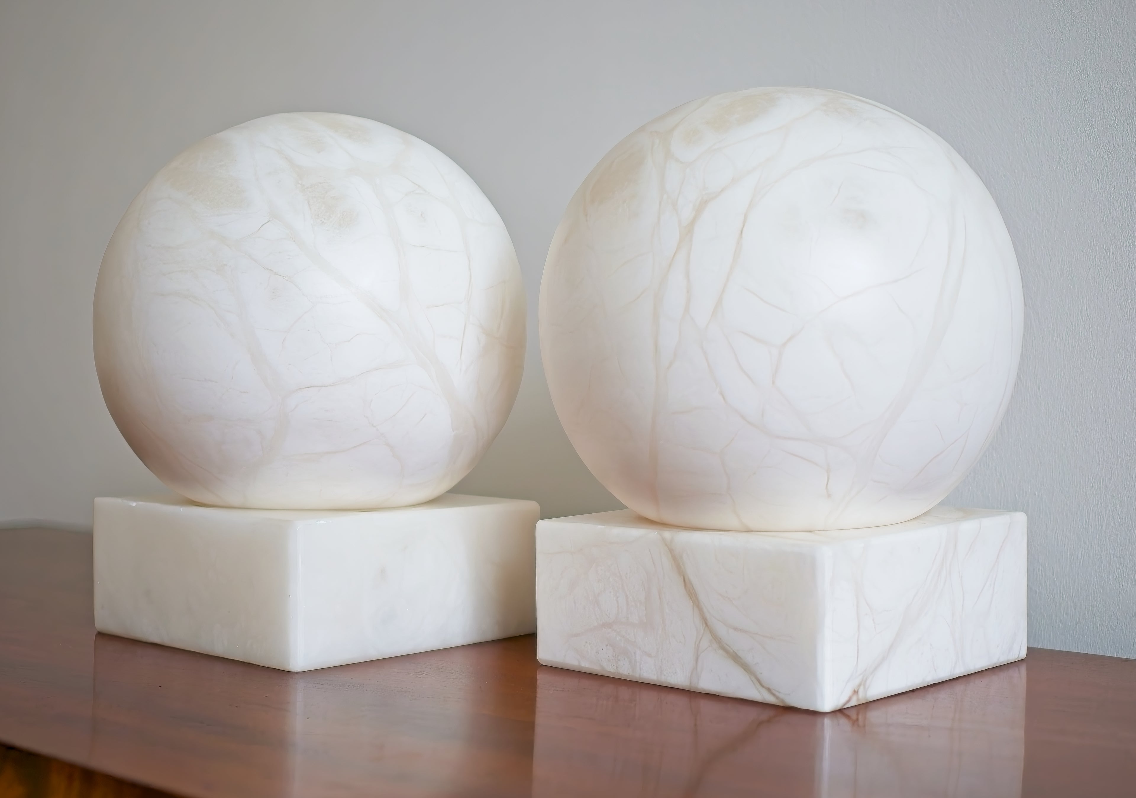 Two white spherical marble lamps with grey vein patterning on square bases against a plain background.
