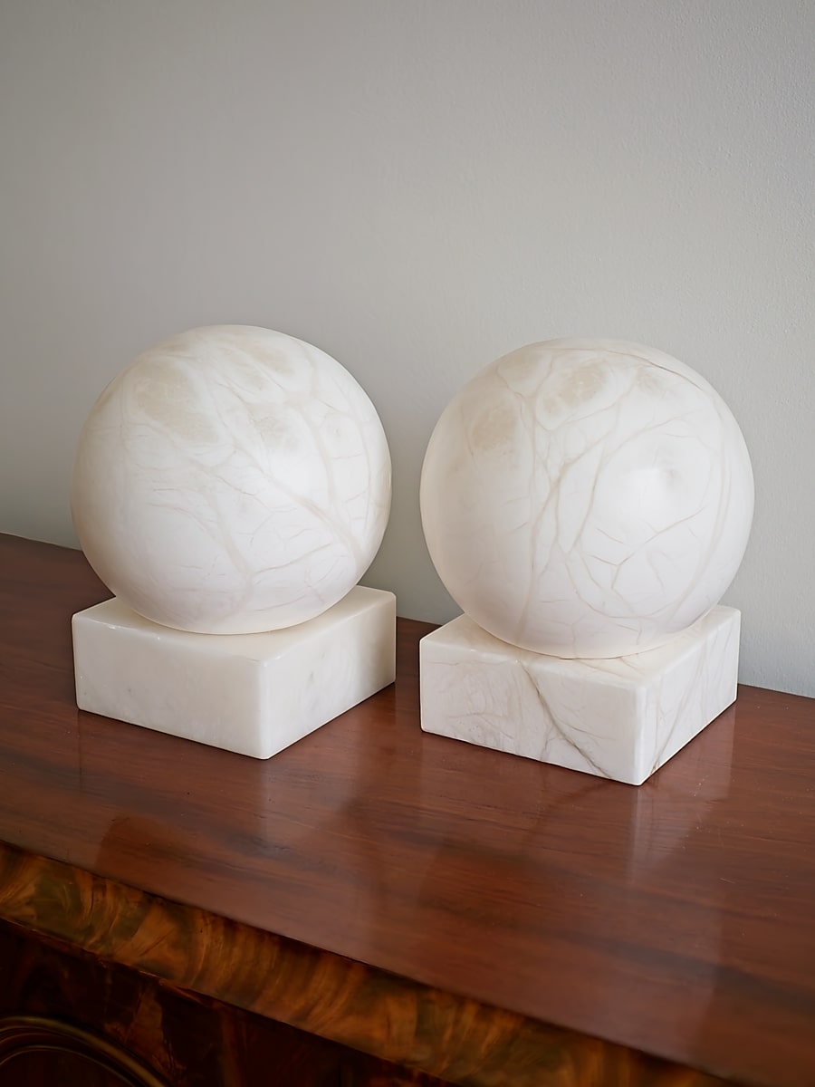 Two marble spherical lamps on square bases against a plain wall.