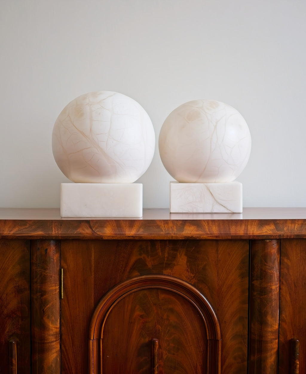Two mid century modern vintage marble sphere table lamps on a wooden cabinet against a white wall