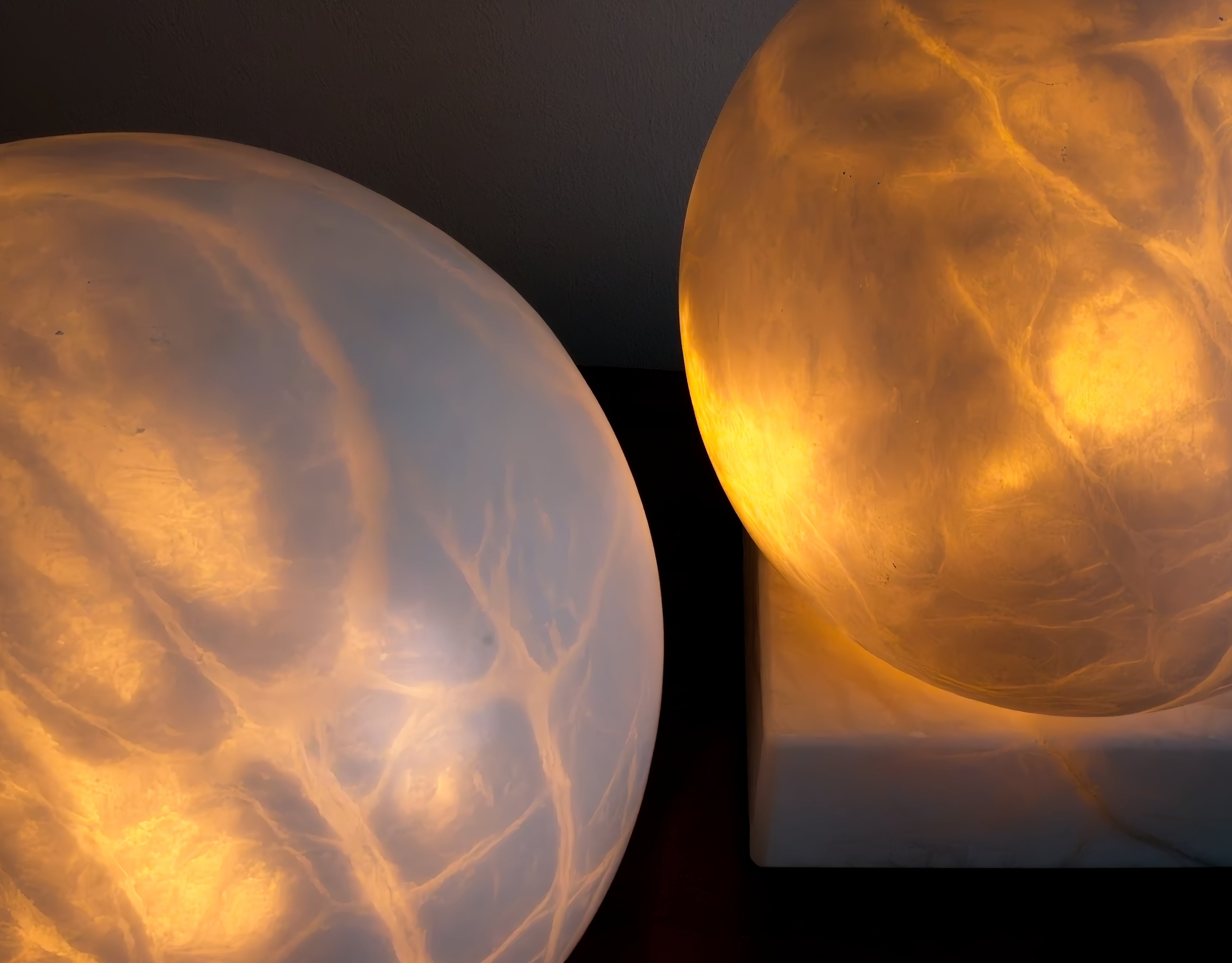 Close up of two glowing white marble spherical sculptural lamps with intricate patterns on a dark background.