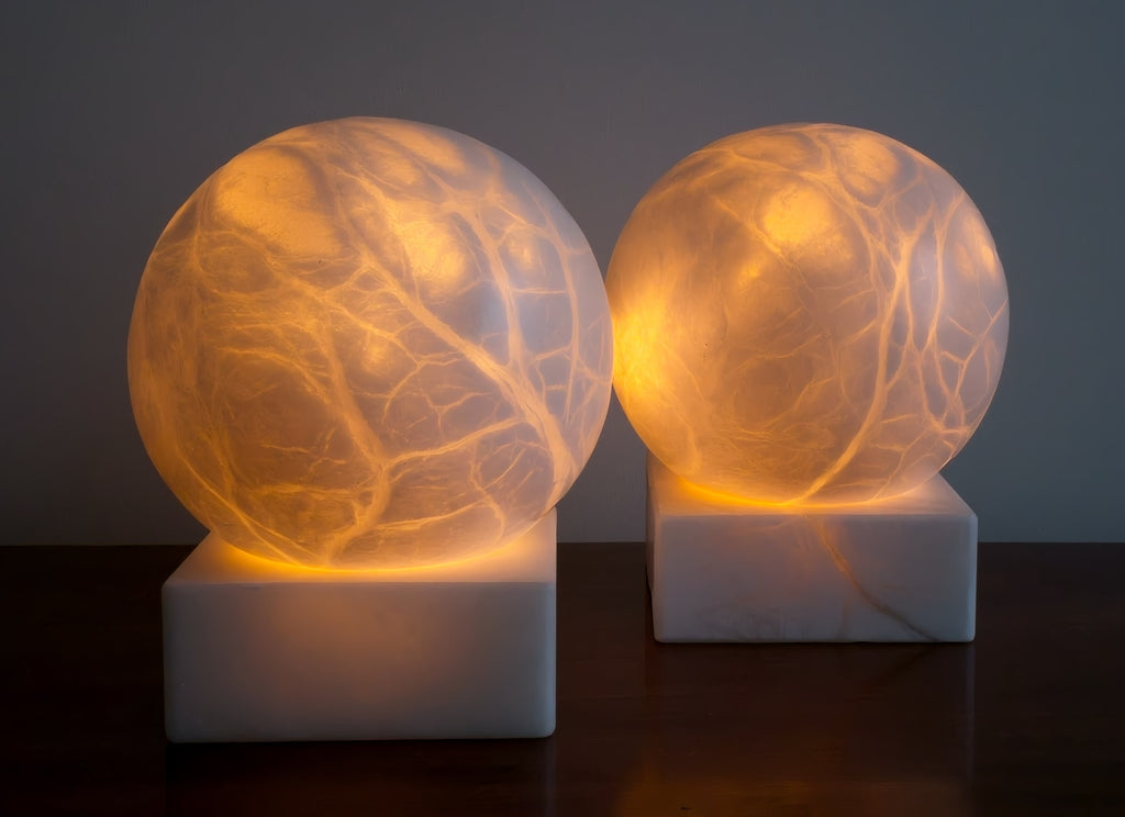 Two mid century modern vintage spherical alabaster marble lamps lit from within with vein-like patterns glowing on a dark background.