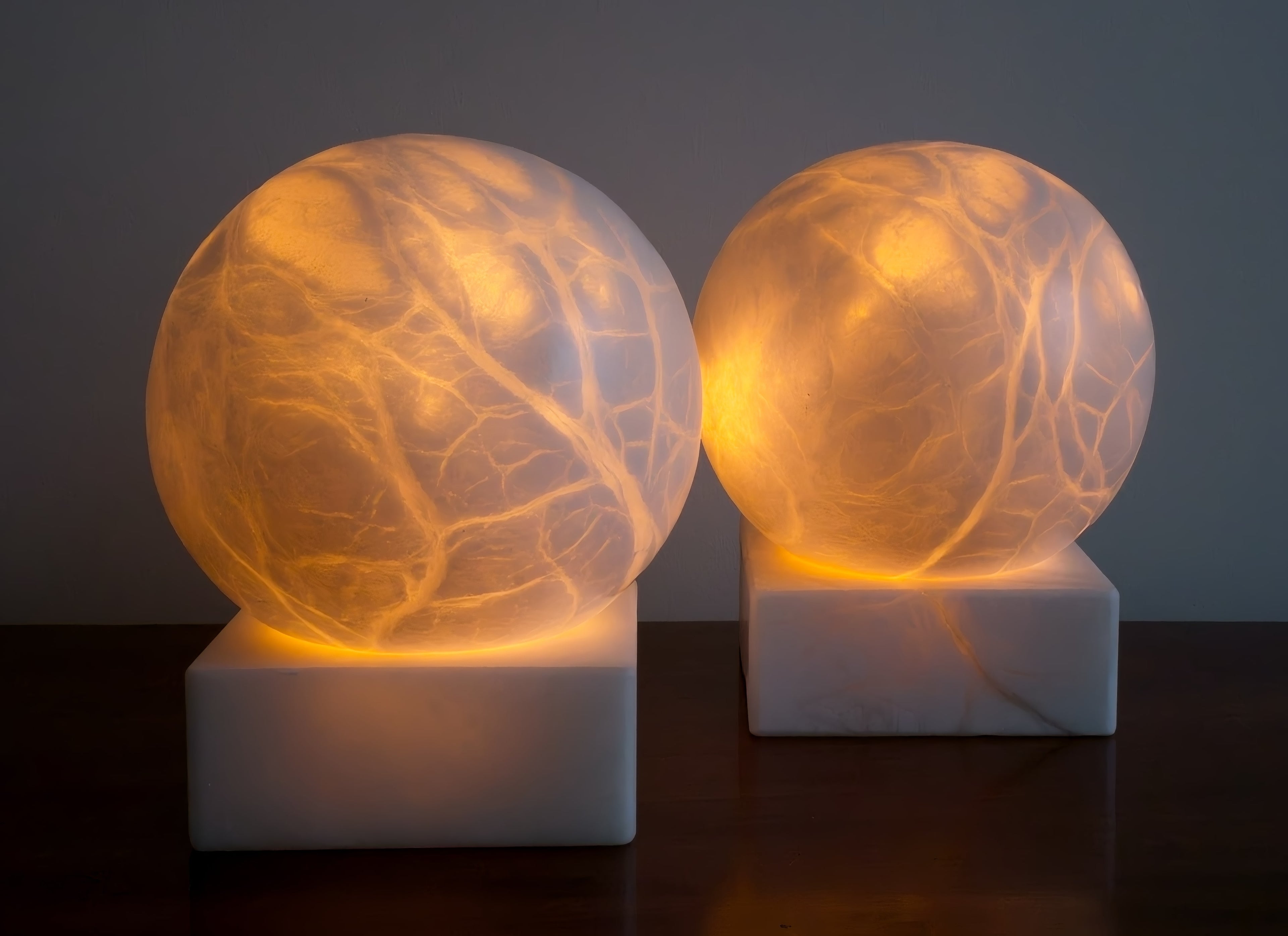Two mid century modern vintage spherical alabaster marble lamps lit from within with vein-like patterns glowing on a dark background.