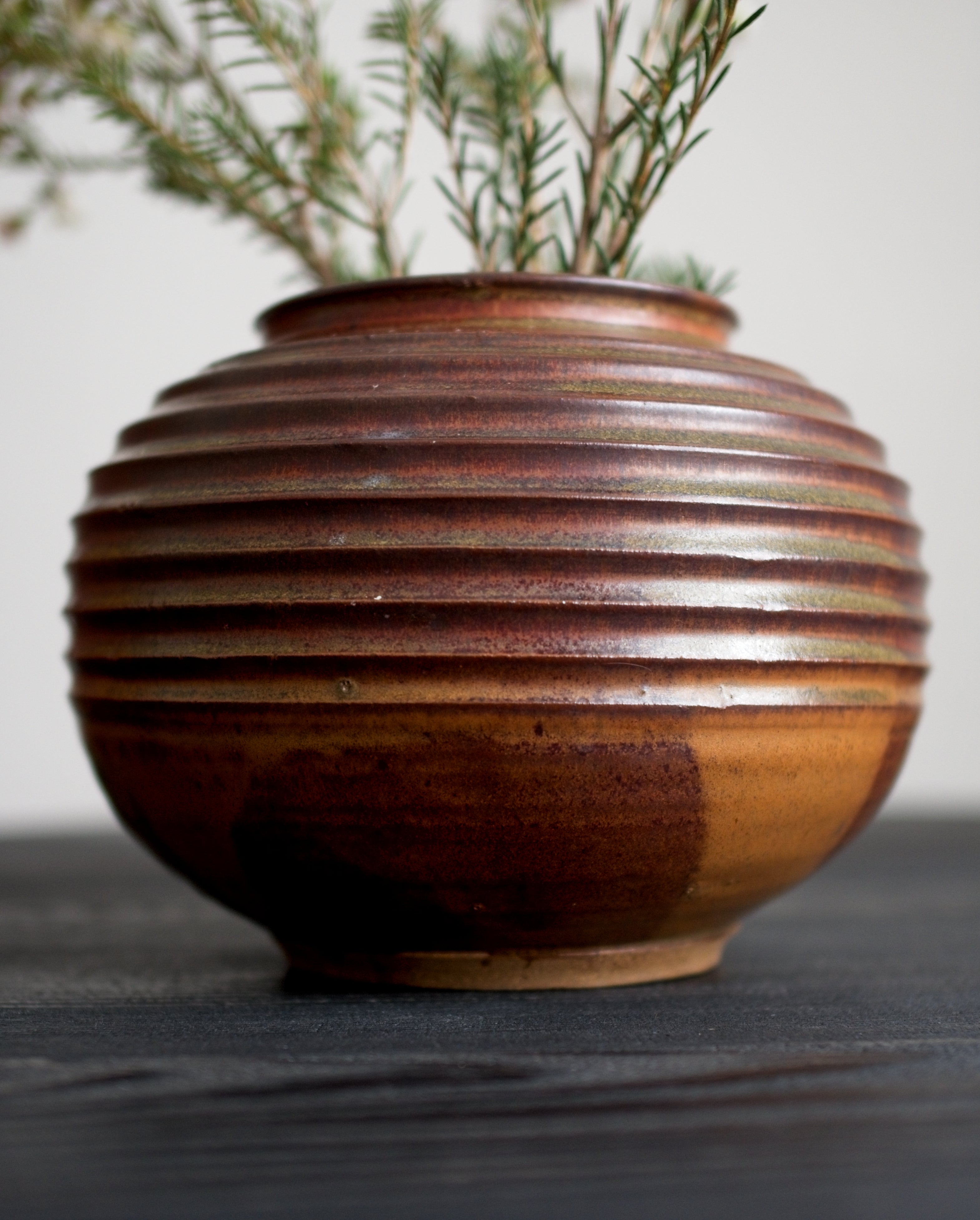 Brown ceramic vase with ribbed texture on a dark wooden surface.