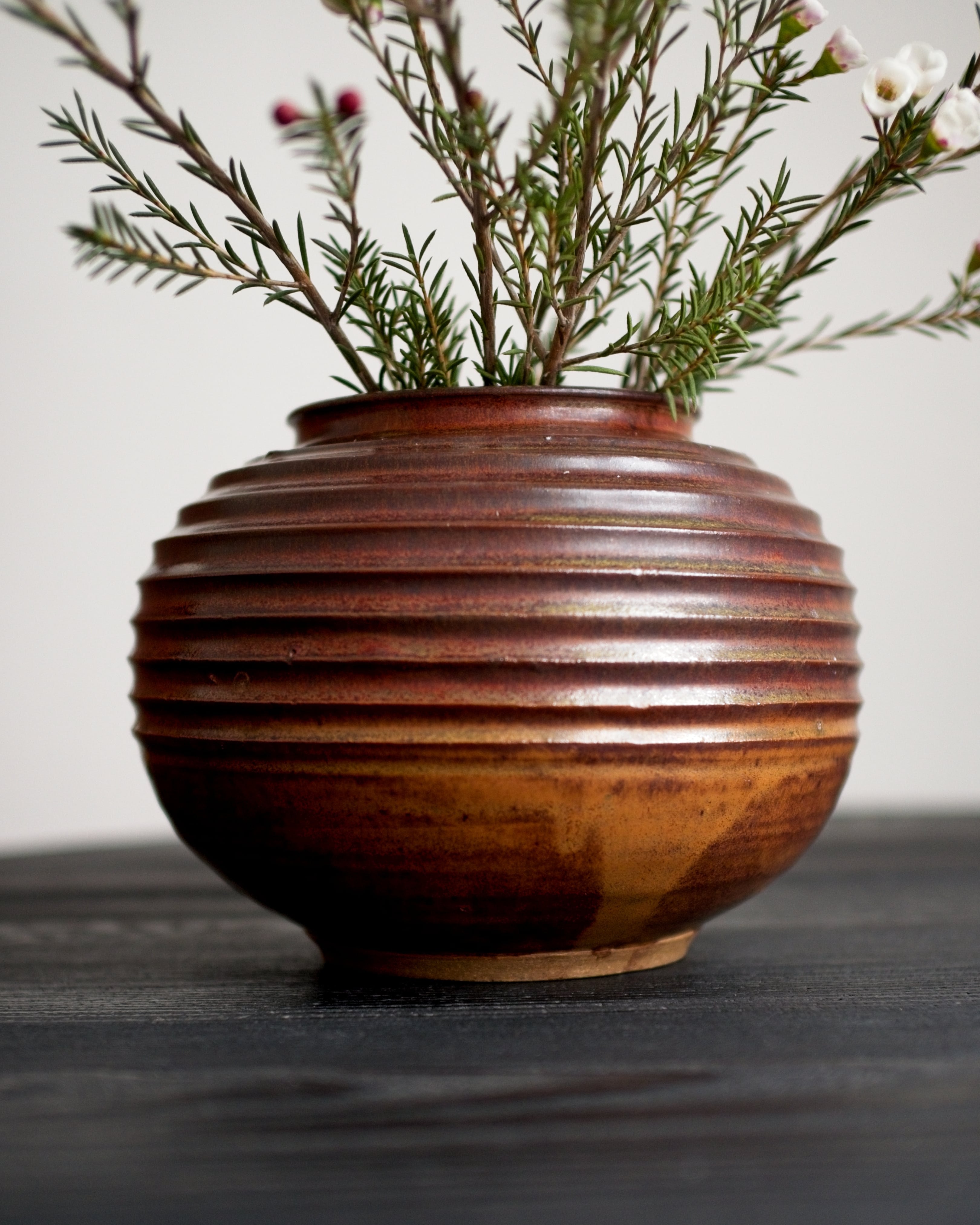 Brown ceramic vase with ribbed texture and orange glaze holding greenery on a dark surface