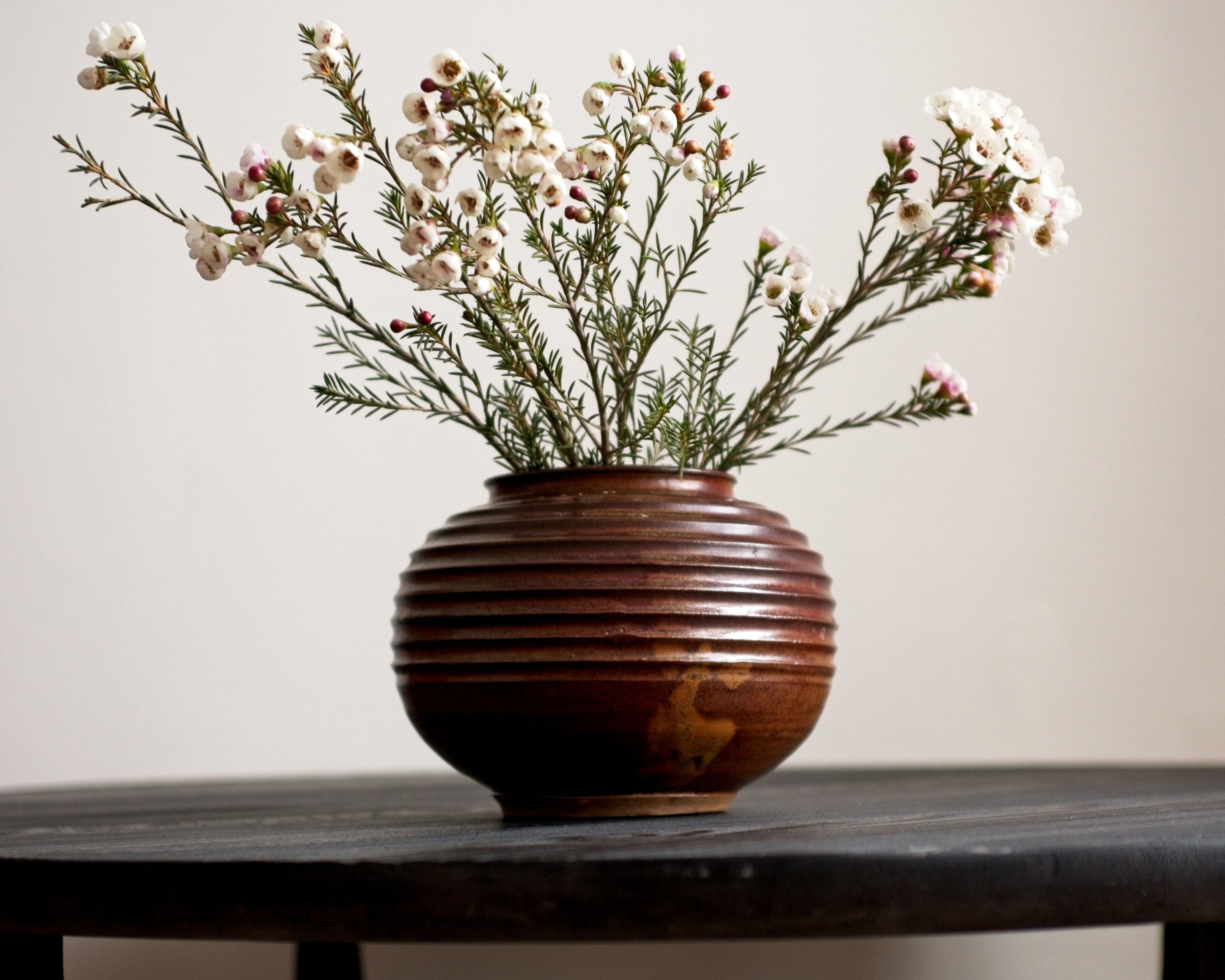 Brown ceramic vase with flowers on a wooden table against a plain background
