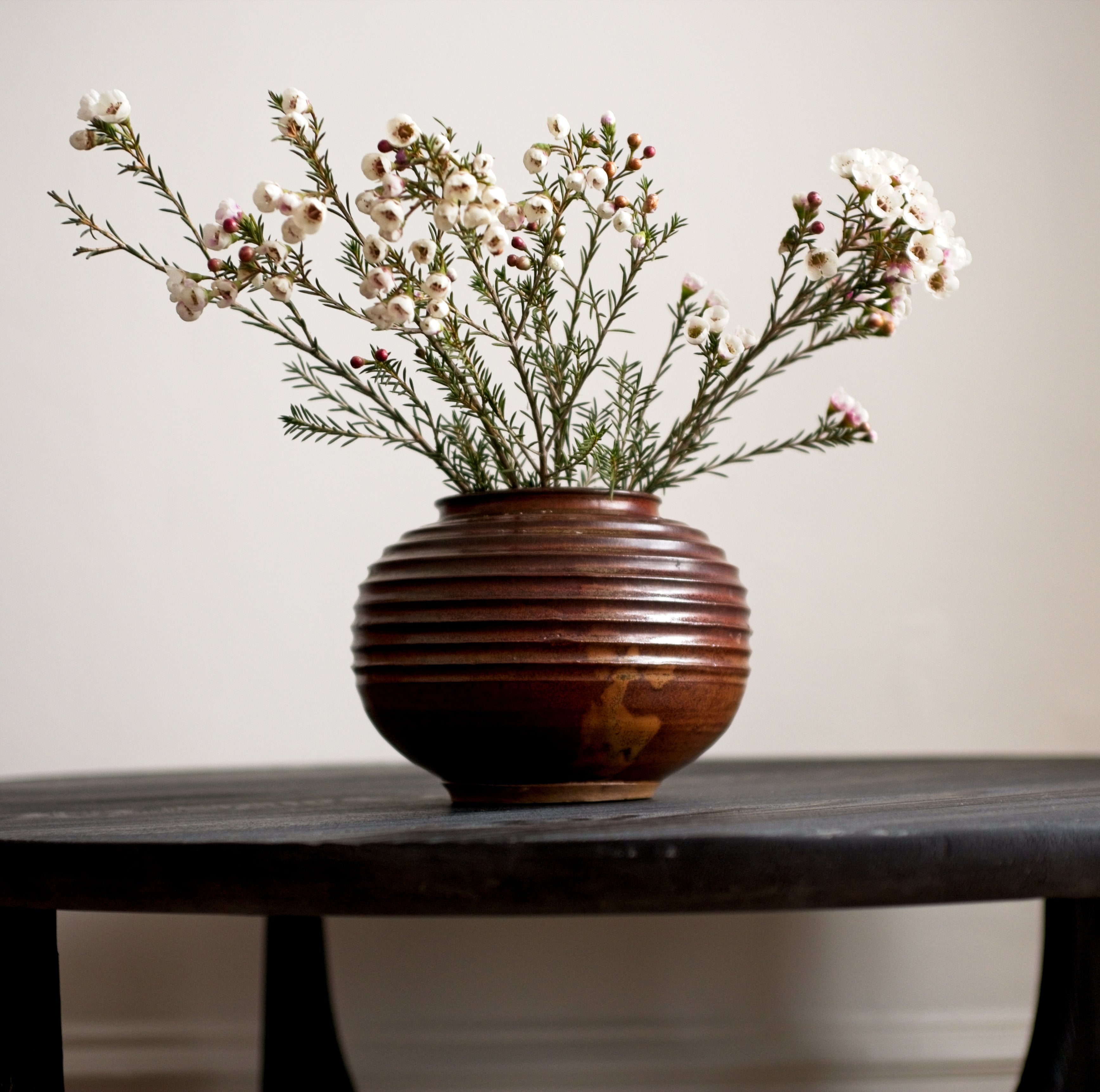 Ceramic vase with small white flowers on a black wooden table against a plain background.