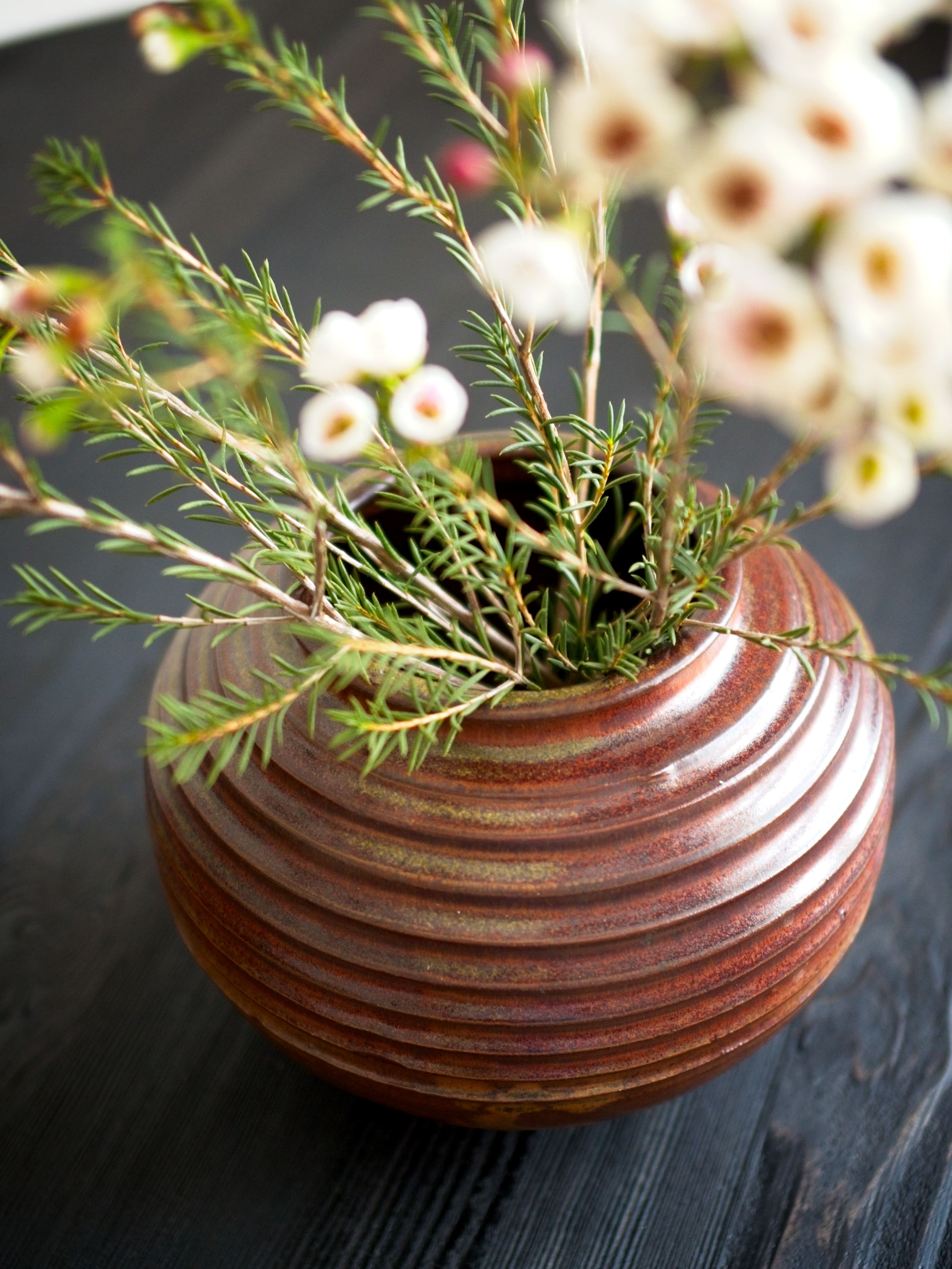Ceramic vase with ribbed texture containing greenery and white flowers on a dark background