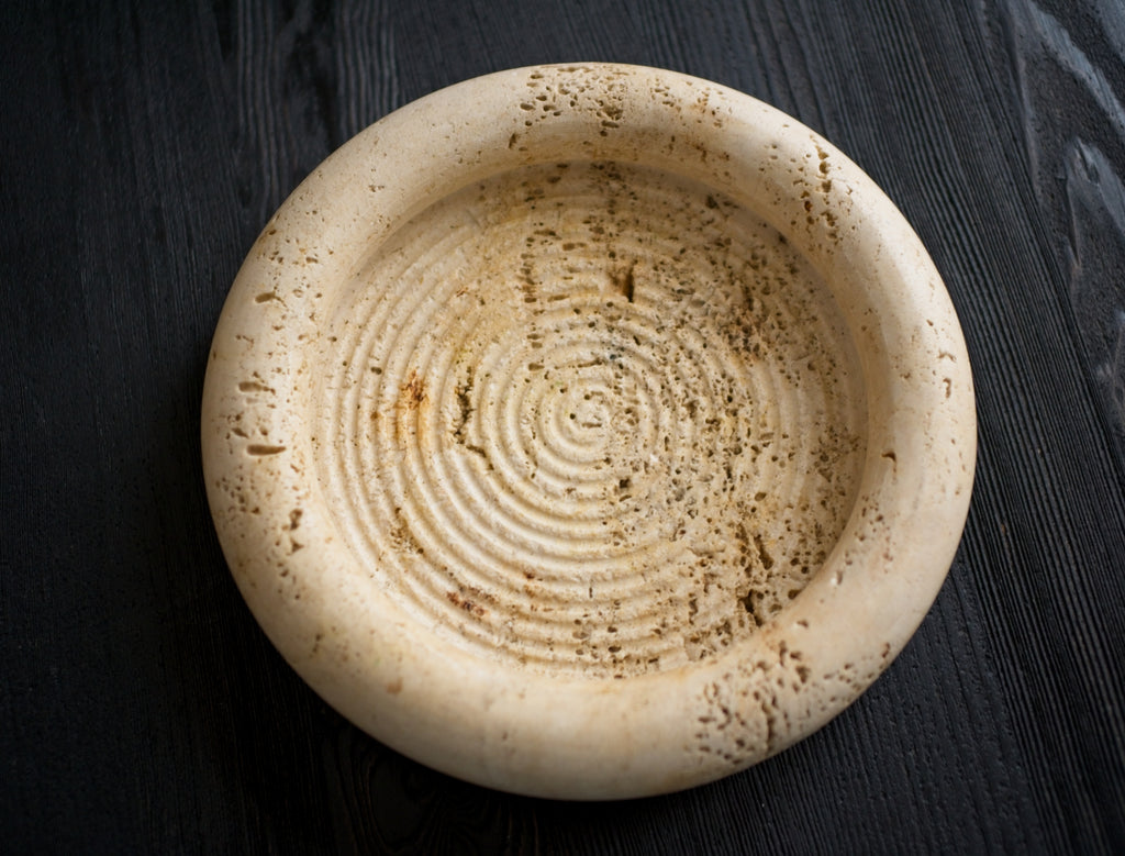 Beige stone plate with textured surface on a black wooden background.