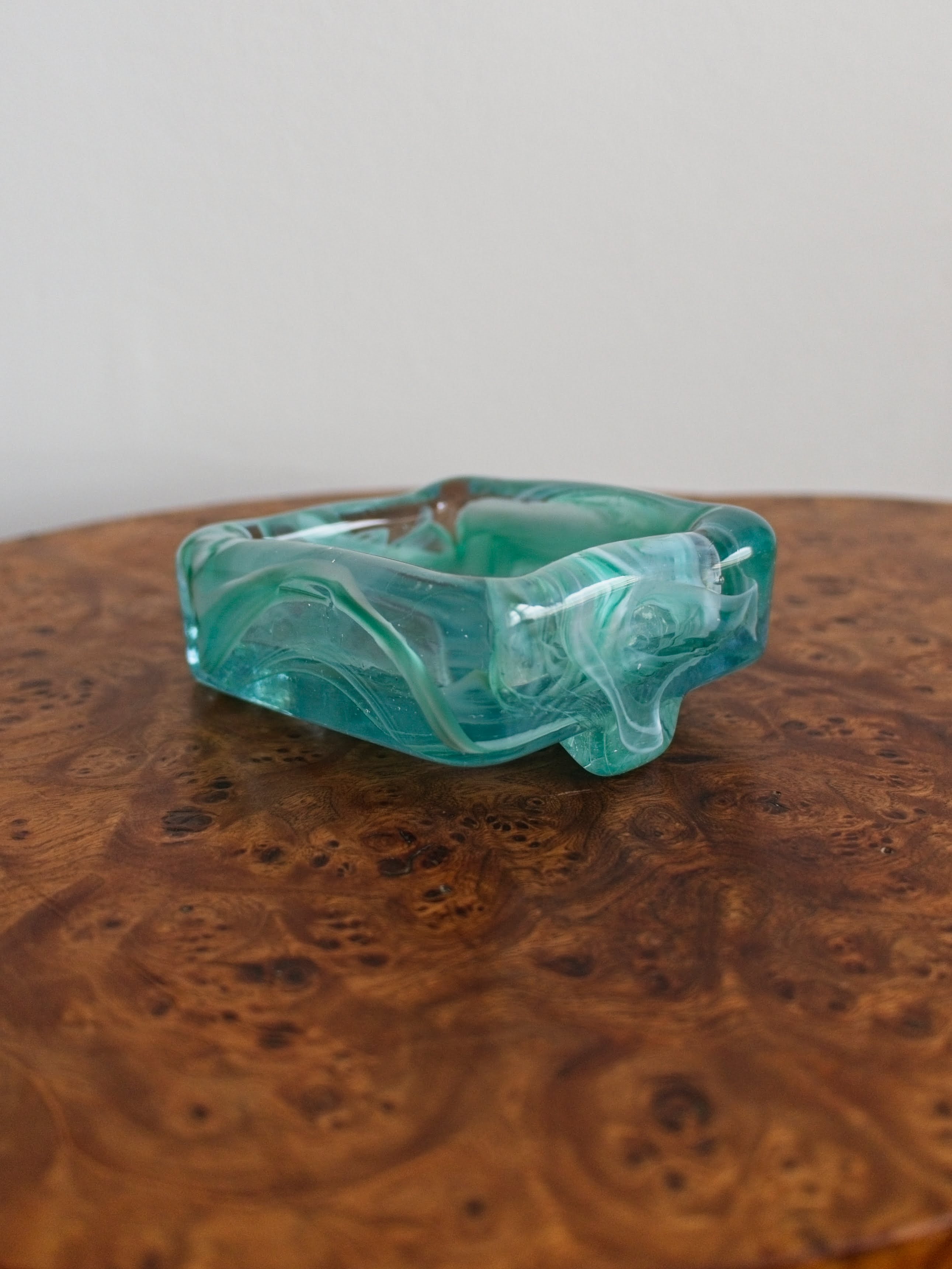 The back side of a small rectangular 1970s mid century modern retro style glass trinket dish with green and white marble swirls similar to Murano glass on a vintage burr wood table.