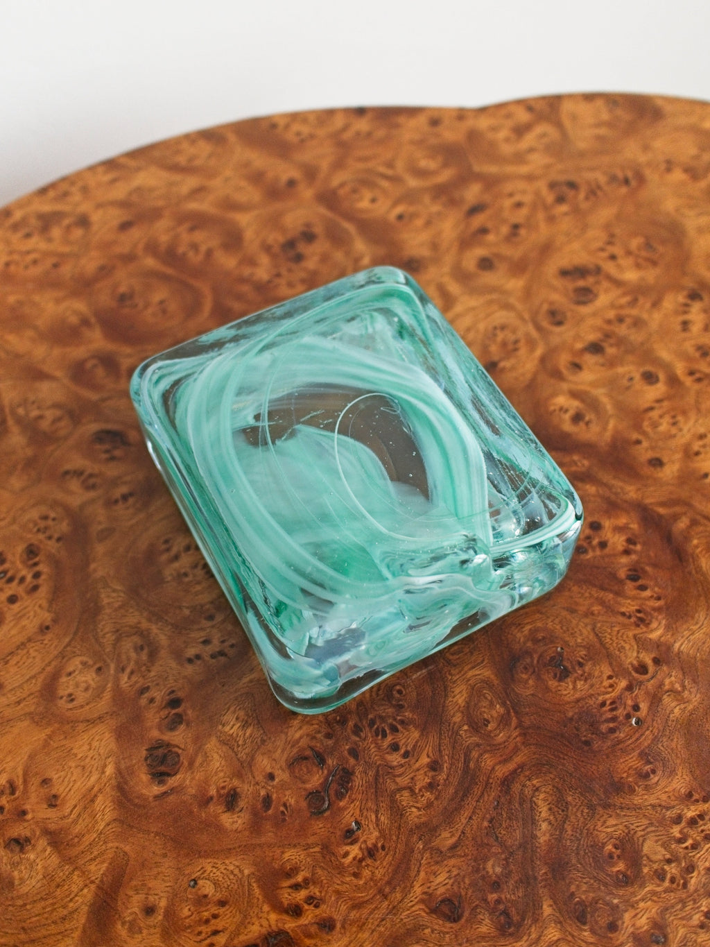 The bottom of a small 1970s mid century modern glass trinket dish with green and white marble swirls similar to Murano glass  on a vintage burr wood table.