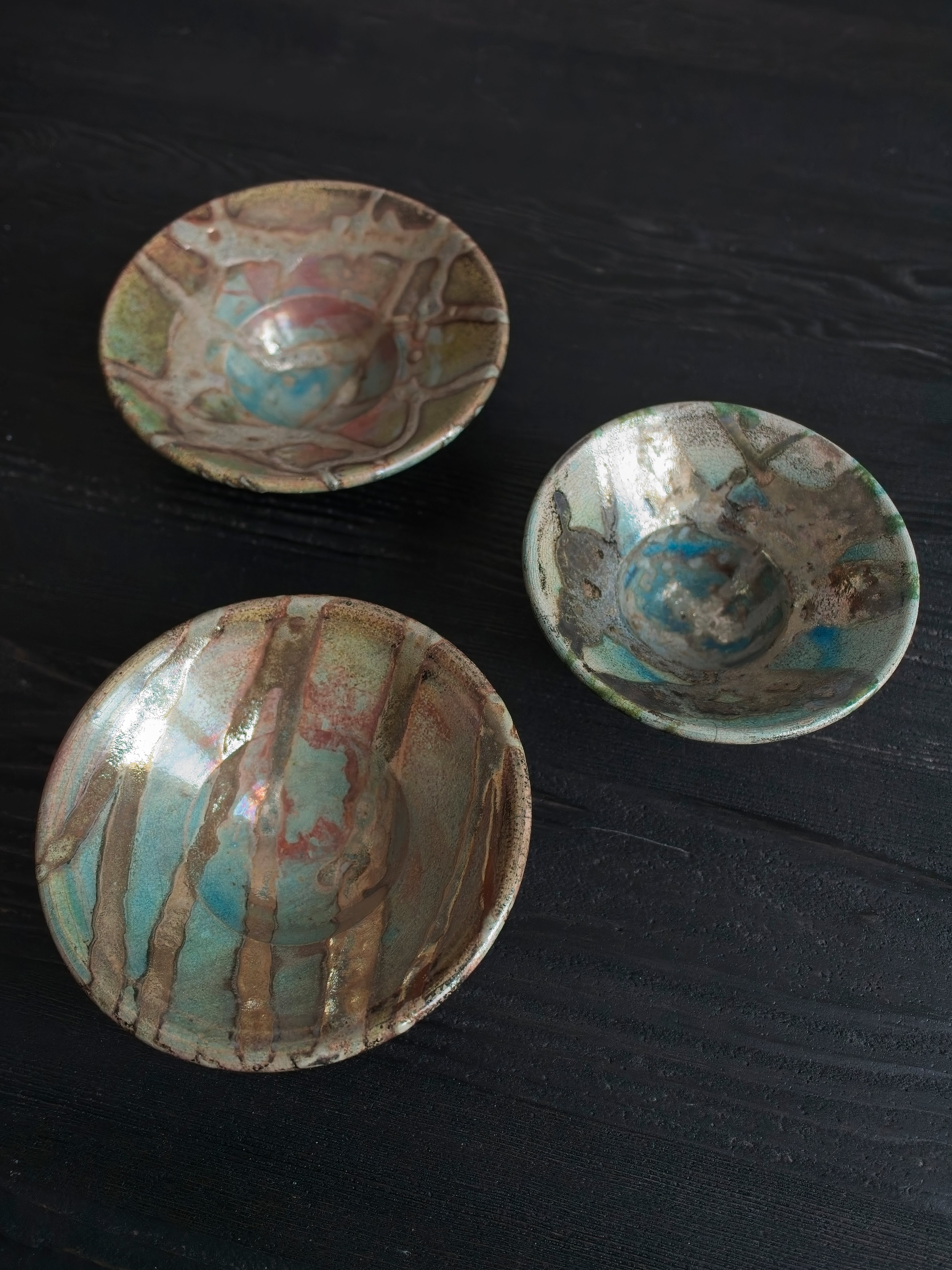 Three mid century style vintage multicoloured Japanese handmade studio pottery ceramic décor bowls with abstract iridescent oxidised glaze patterns on a black wood surface.