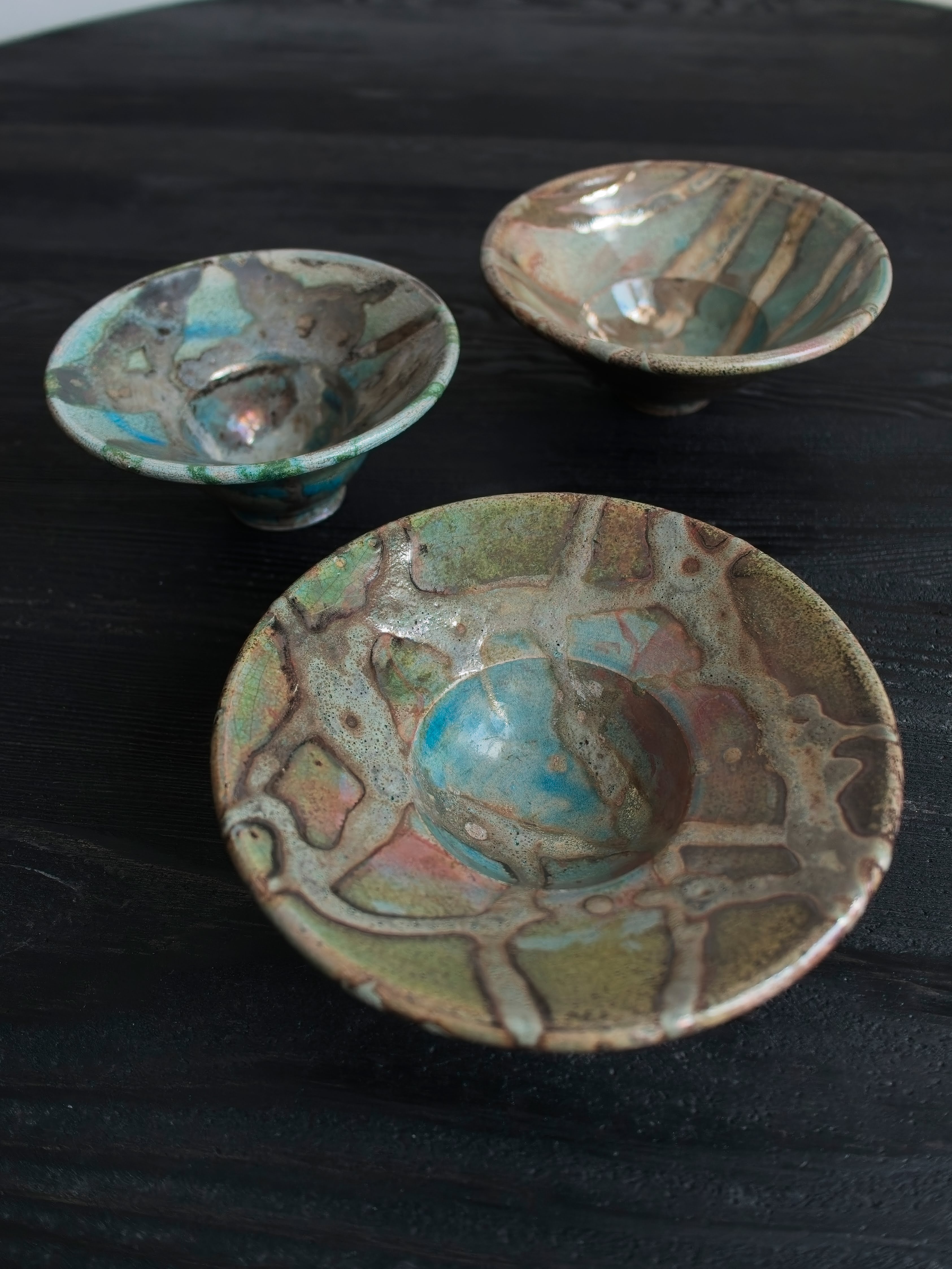 Three vintage Japanese raku handmade studio pottery ceramic décor bowls with abstract oxidised iridescent glaze patterns on a black wooden table.