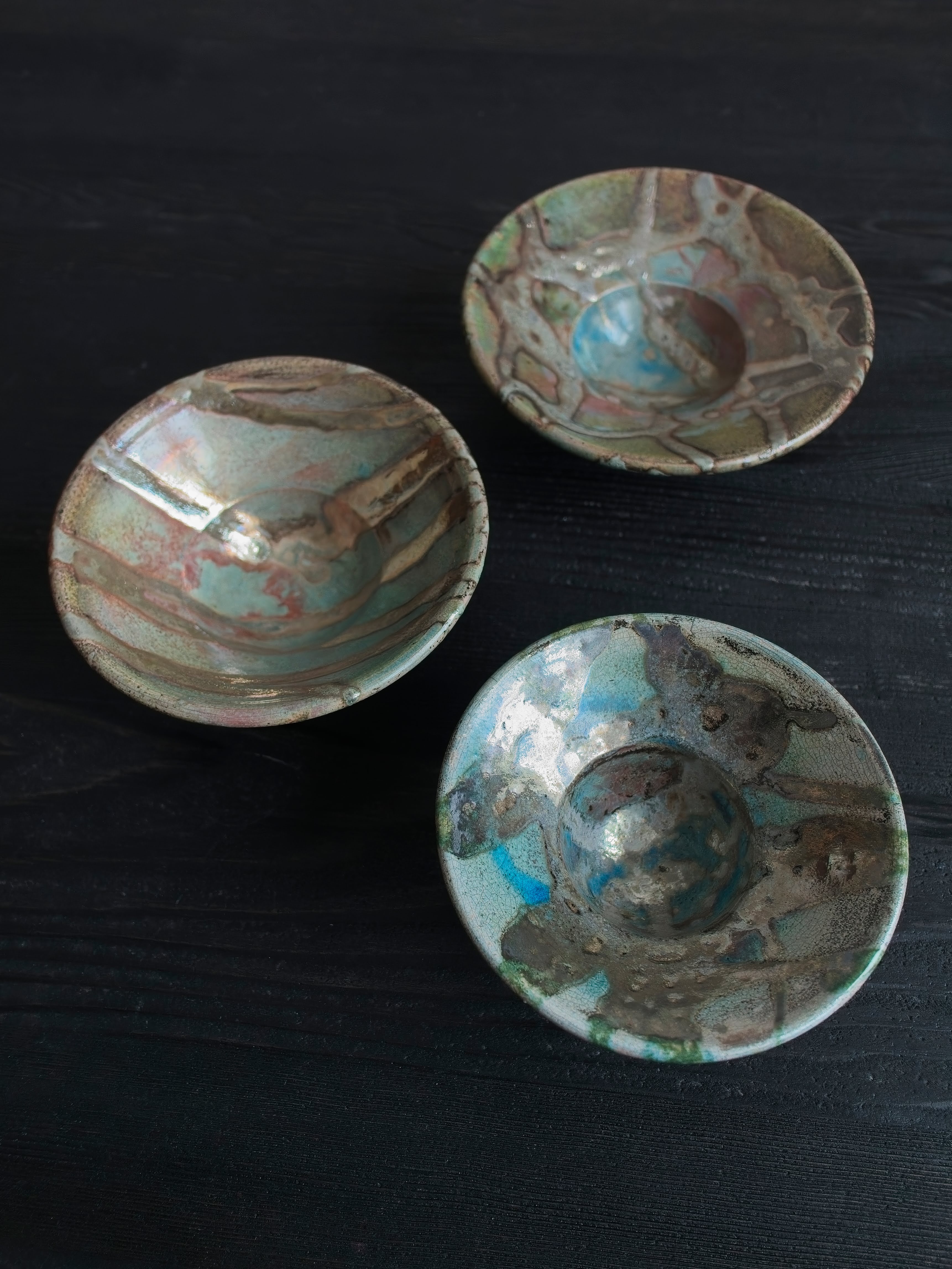 Three vintage multicoloured Japanese handmade ceramic studio pottery décor bowls with abstract oxidised glaze patterns on a black wooden table.