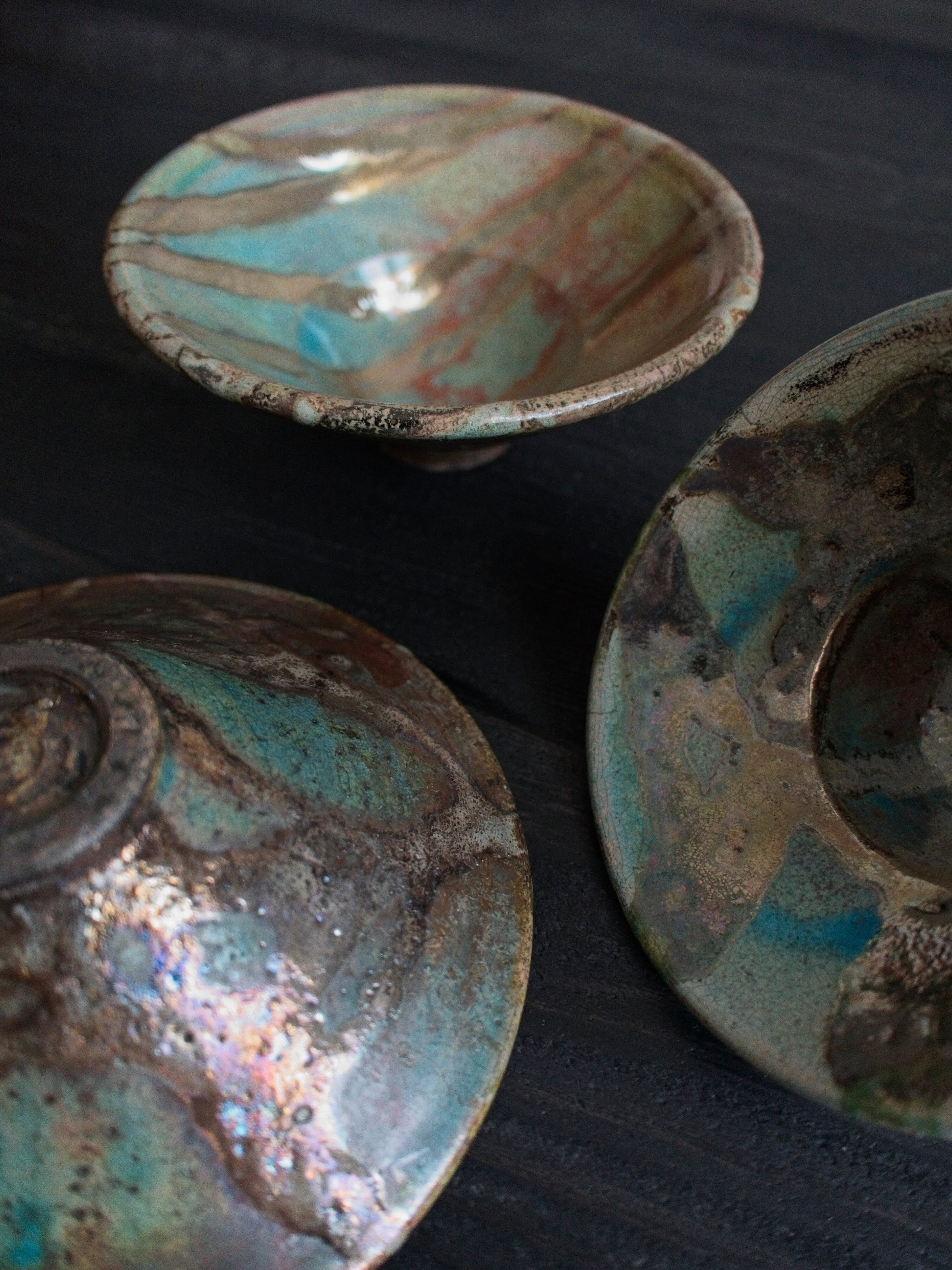 A close up of three vintage ceramic multicoloured Japanese handmade studio pottery décor bowls with abstract oxidise iridescent glaze patterns on a black wooden table.