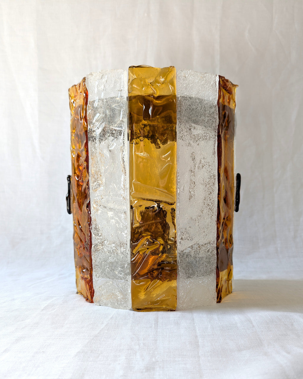 A vintage mid century modern 1970s Carlo Nason for Mazzega rectangular wall sconce with textured amber and clear striped Murano glass panels on white linen surface.