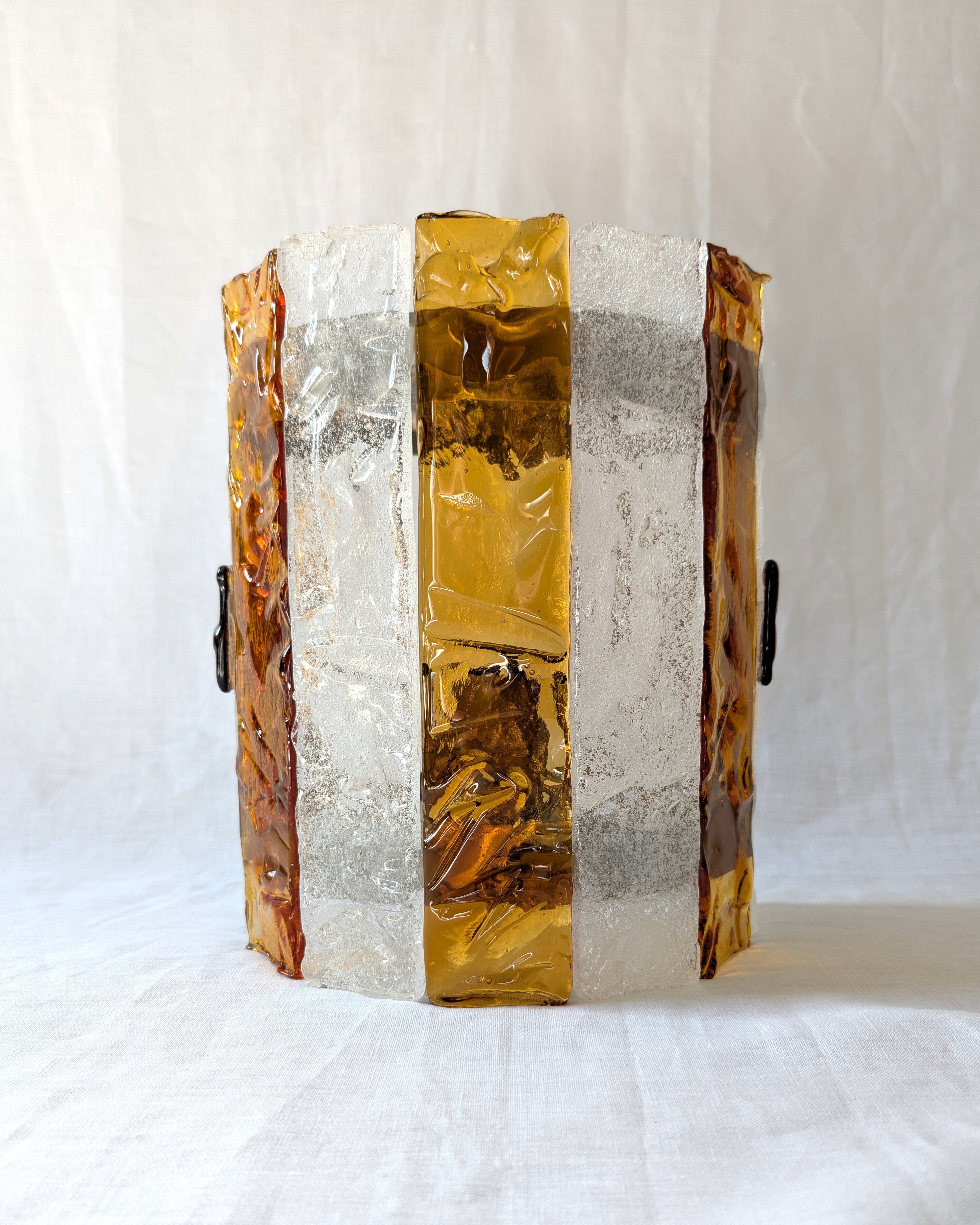 A vintage mid century modern 1970s Carlo Nason for Mazzega rectangular wall sconce with textured amber and clear striped Murano glass panels on white linen surface.