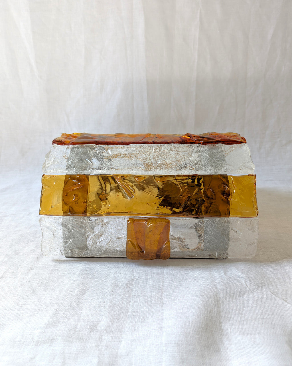A vintage mid century modern 1970s Carlo Nason for Mazzega rectangular wall sconce with textured amber and clear striped Murano glass panels lying on its side to show a curved profile on white linen surface.