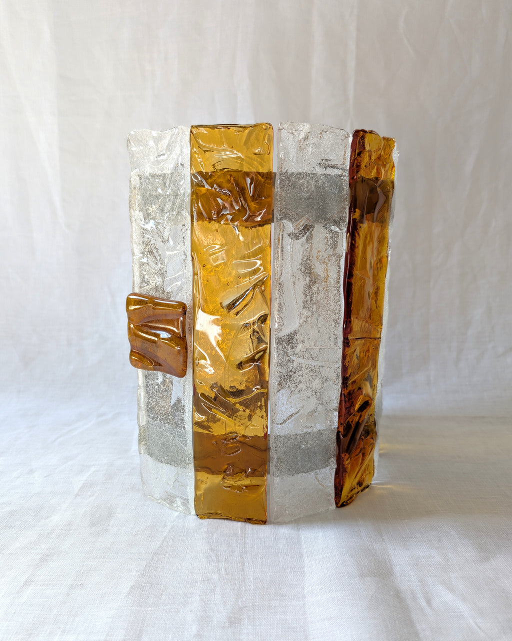 the side of a vintage mid century modern 1970s Carlo Nason for Mazzega rectangular wall sconce with textured amber and clear striped Murano glass panels on white linen surface.