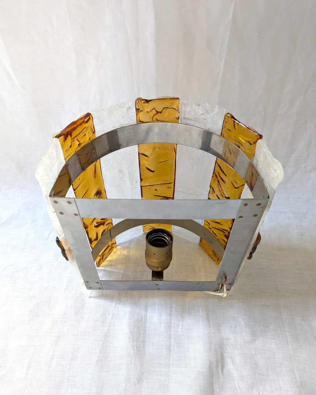 The back of a vintage mid century modern 1970s Carlo Nason for Mazzega rectangular wall sconce showing the metal hanging bracket, light bulb socket and wiring, with textured amber and clear striped Murano glass panels on white linen surface.