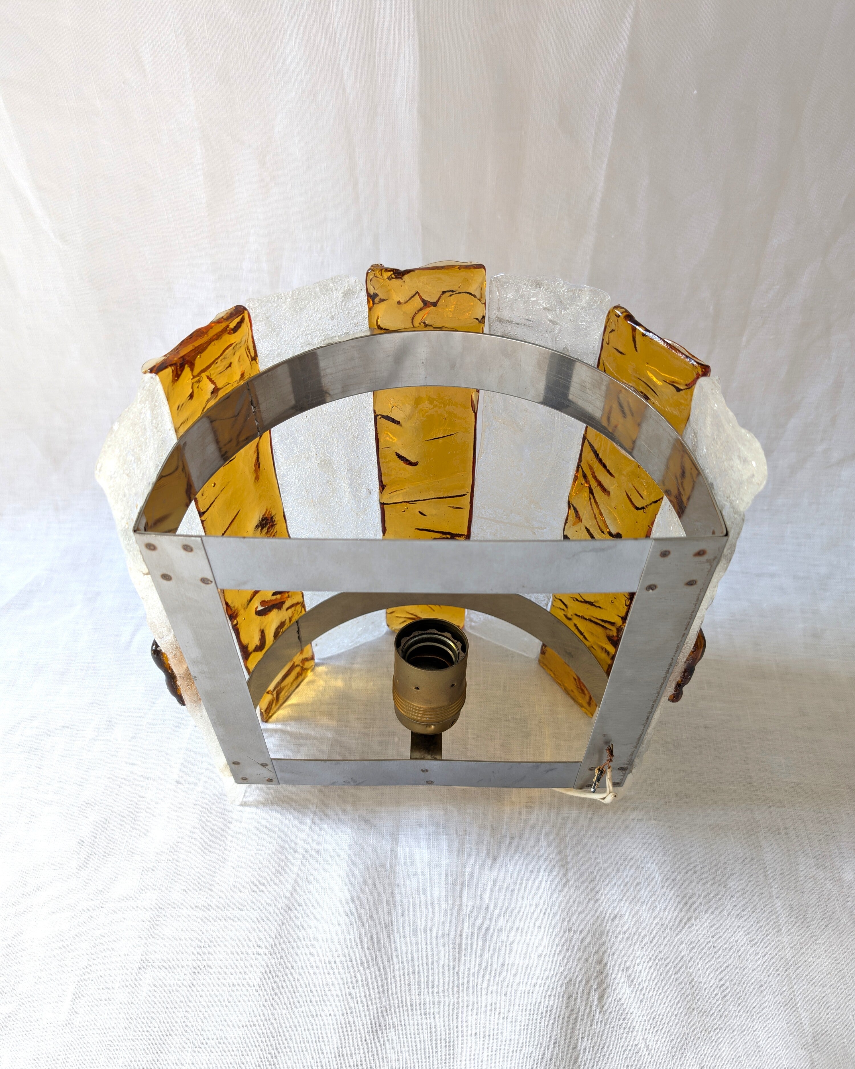 The back of a vintage mid century modern 1970s Carlo Nason for Mazzega rectangular wall sconce showing the metal hanging bracket, light bulb socket and wiring, with textured amber and clear striped Murano glass panels on white linen surface.