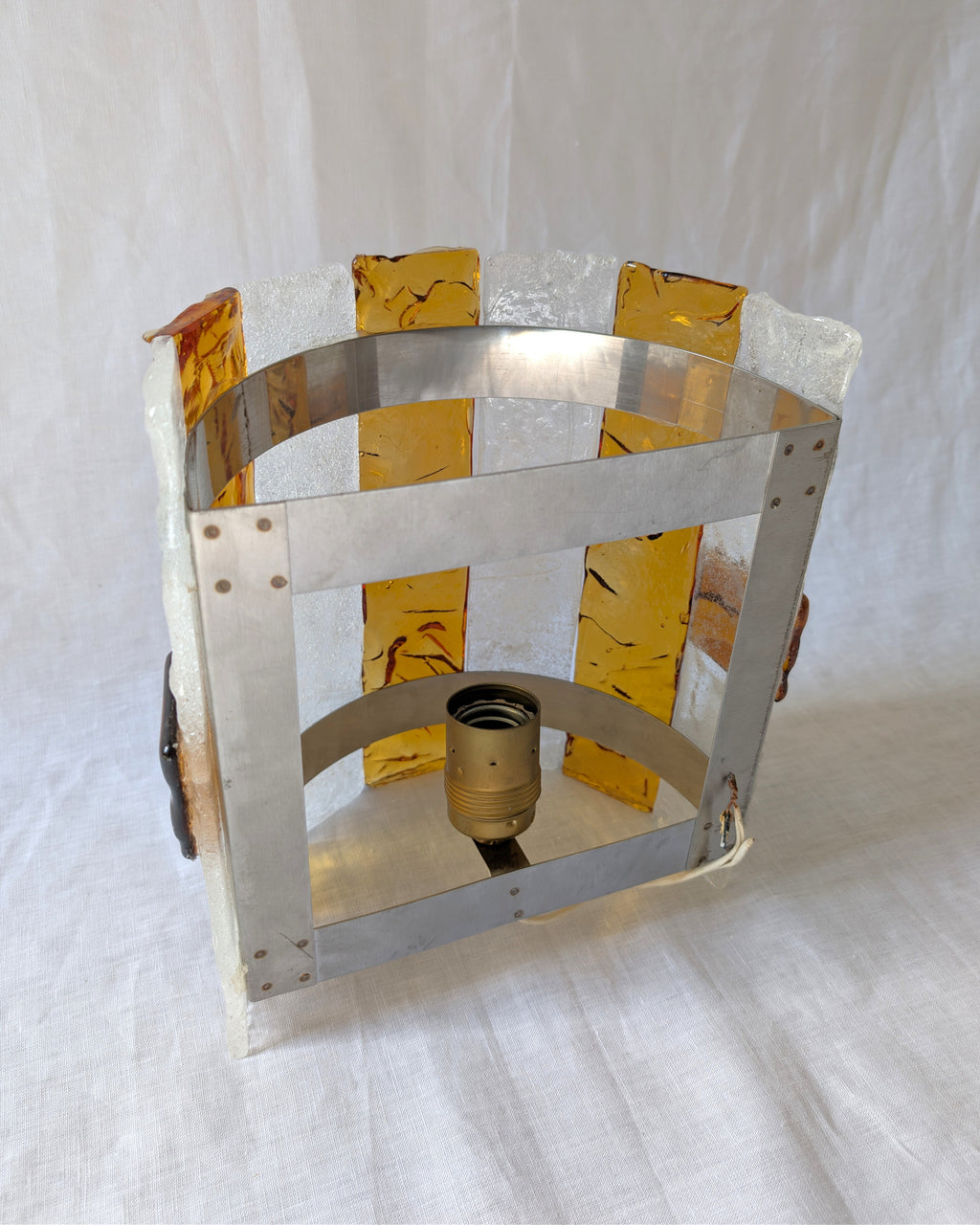 The back of a vintage mid century modern 1970s Carlo Nason for Mazzega rectangular wall sconce showing the metal hanging bracket, light bulb socket and wiring, with textured amber and clear striped Murano glass panels on white linen surface.