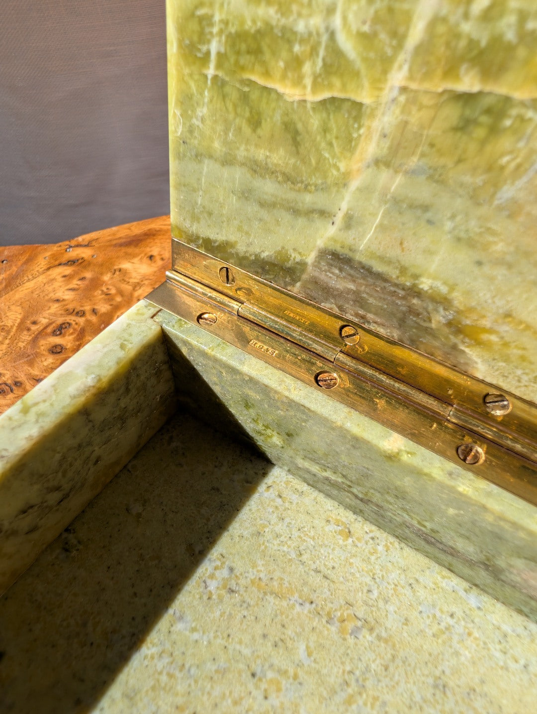 A close up of the makers engraving on the hinge of an antique green marble decor box by Henry Griffith & Sons, open to show the inside, on a Hollywood Regency style burl wood table. This rare Victorian decor box, made from hand carved solid Italian marble similar to onyx or jade, can be used as a trinket box, jewellery holder or cigar box and would be a beautiful addition to a vintage eclectic, mid century modern, minimalist, modernist, maximalist, baroque or art deco home interior schemes.