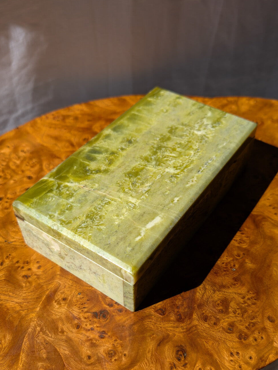A close up of the top of an antique green marble decor box by Henry Griffith & Sons, open to show the inside, on a Hollywood Regency style burl wood table. This rare Victorian decor box, made from hand carved solid Italian marble similar to onyx or jade, can be used as a trinket box, jewellery holder or cigar box and would be a beautiful addition to a vintage eclectic, mid century modern, minimalist, modernist, maximalist, baroque or art deco home interior schemes.