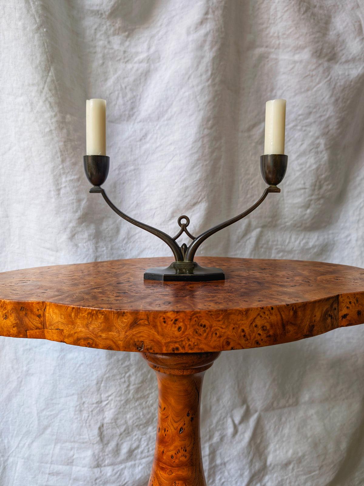 A 1930s art deco bronze candleholder by Danish mid century modern designer Just Andersen on an antique burl wood table in front of a white backdrop. This vintage modernist candlestick is dark bronze with patina, has a carved central motif and octagonal base and two arms. This Scandinavian candle holder would blend seamlessly in minimalist, modern vintage, eclectic, retro, maximalist, baroque or cottage farmhouse home interiors.