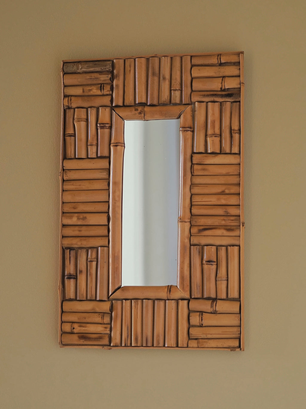 A vintage 1970s wall mounted bamboo mirror by UK modernist vintage home décor store Vintrovia. This mid century modern rectangular mirror hangs on a muted yellow wall and is skillfully hand crafted using individual honey-toned rattan pieces to form a geometric check design that creates an interesting, modernist aesthetic. A versatile retro wall décor piece that would elevate boho, eclectic, coastal and rustic home interior schemes.