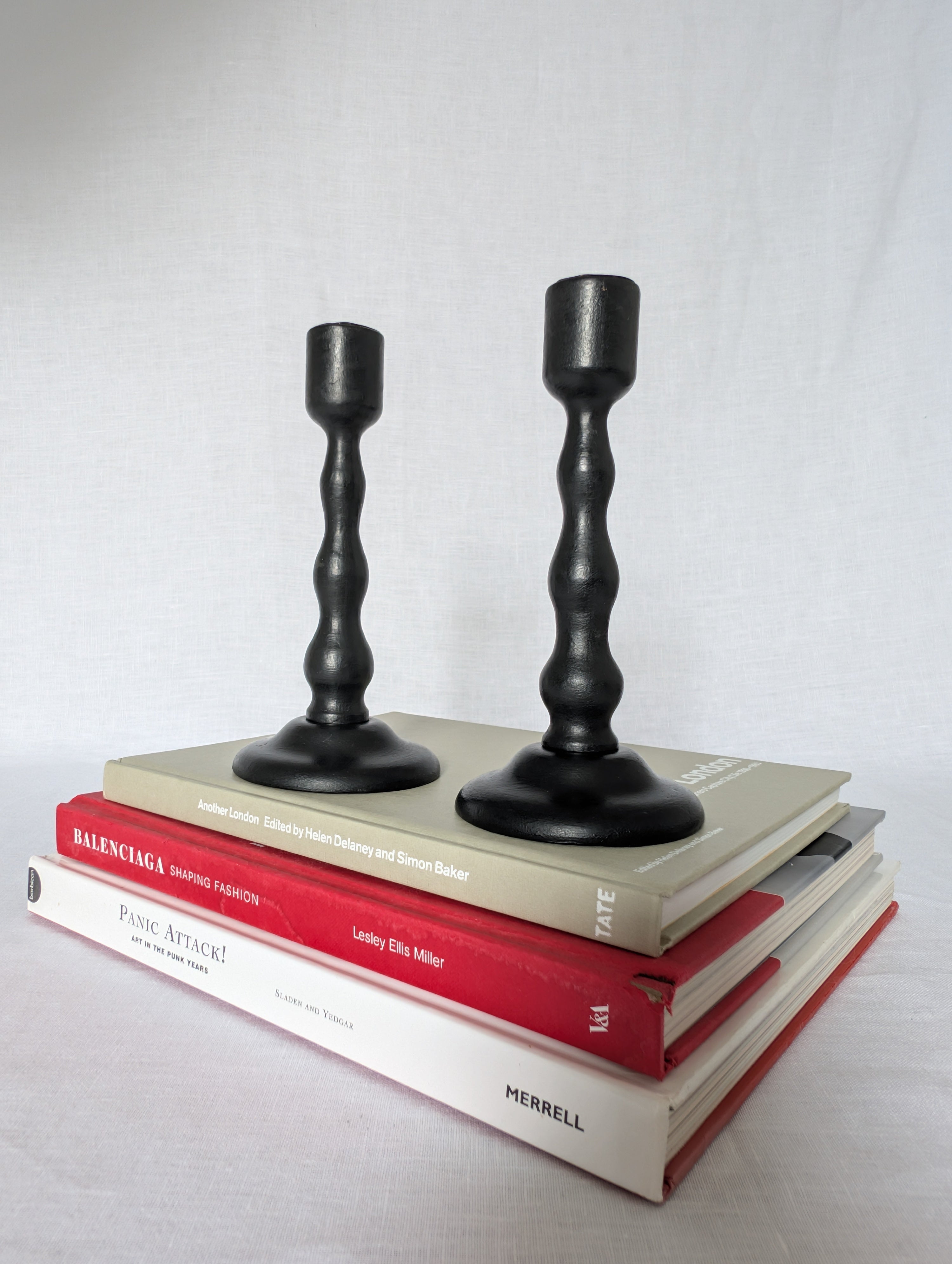 Two black candlesticks on top of books with a plain background