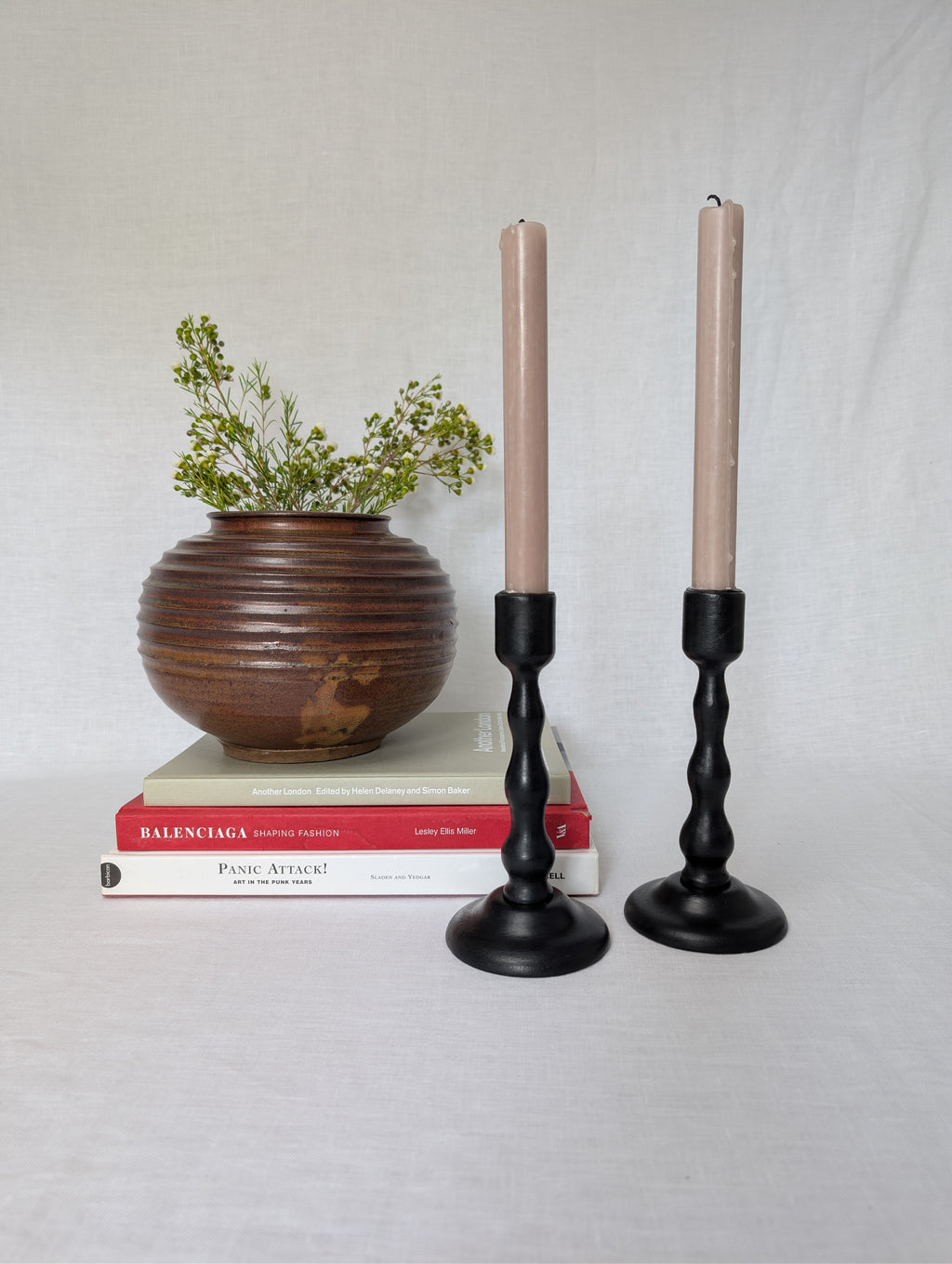 Two candlesticks with candles, a wooden vase with greenery, and books on a light gray background