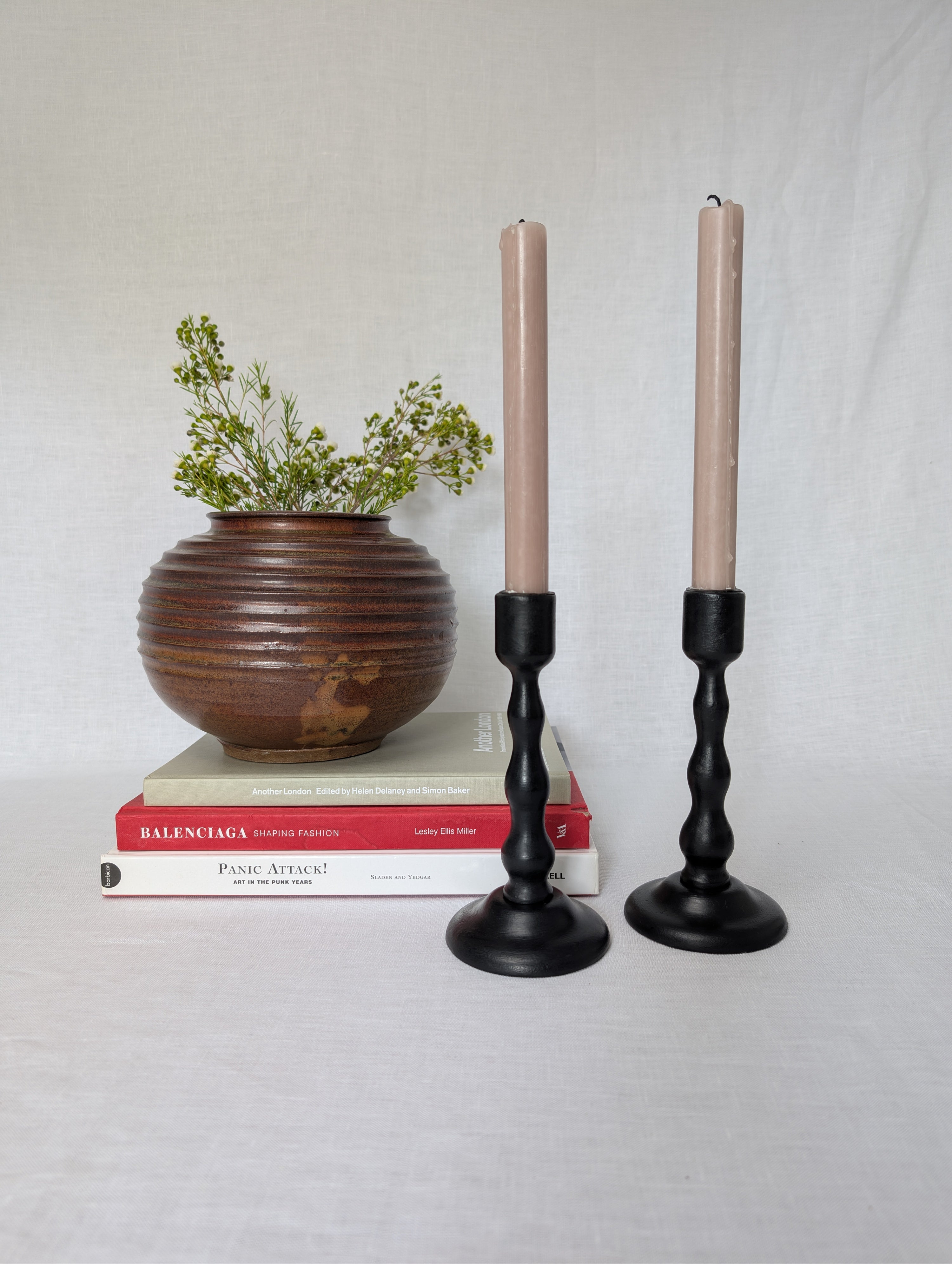 Two candlesticks with candles, a wooden vase with greenery, and books on a light gray background