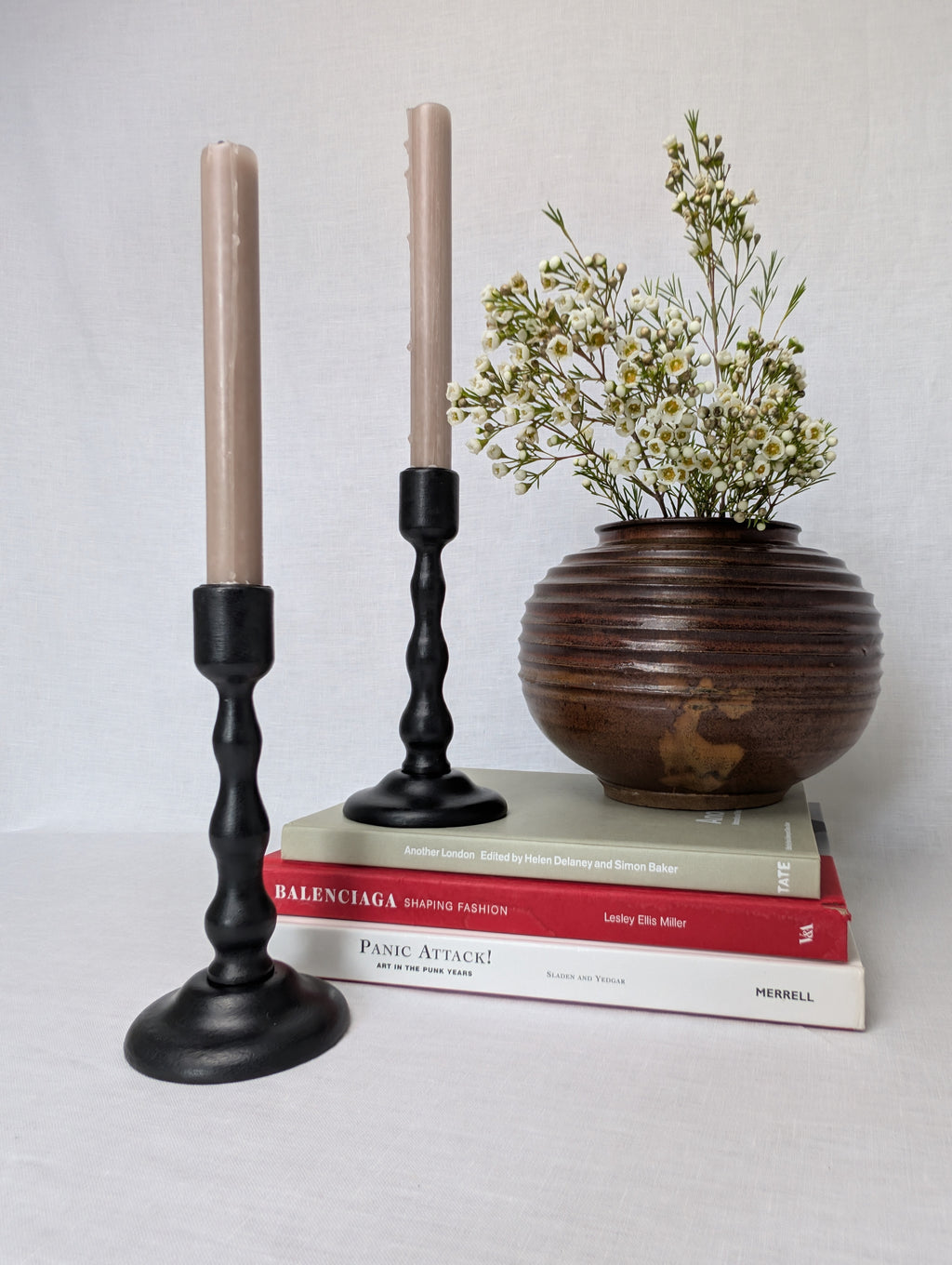 Decorative candlesticks with a vase of flowers on books against a plain background