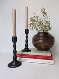 Decorative candlesticks with a vase of flowers on books against a plain background