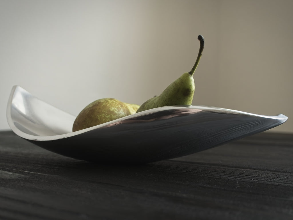 Two green pears on a mid century modern vintage freeform silver dish against a beige background.