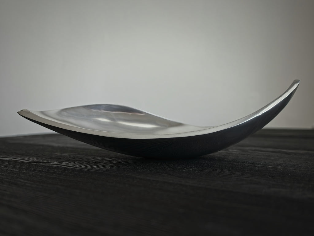 A mid century modern vintage sculptural silver home décor dish on a dark surface with a neutral background.