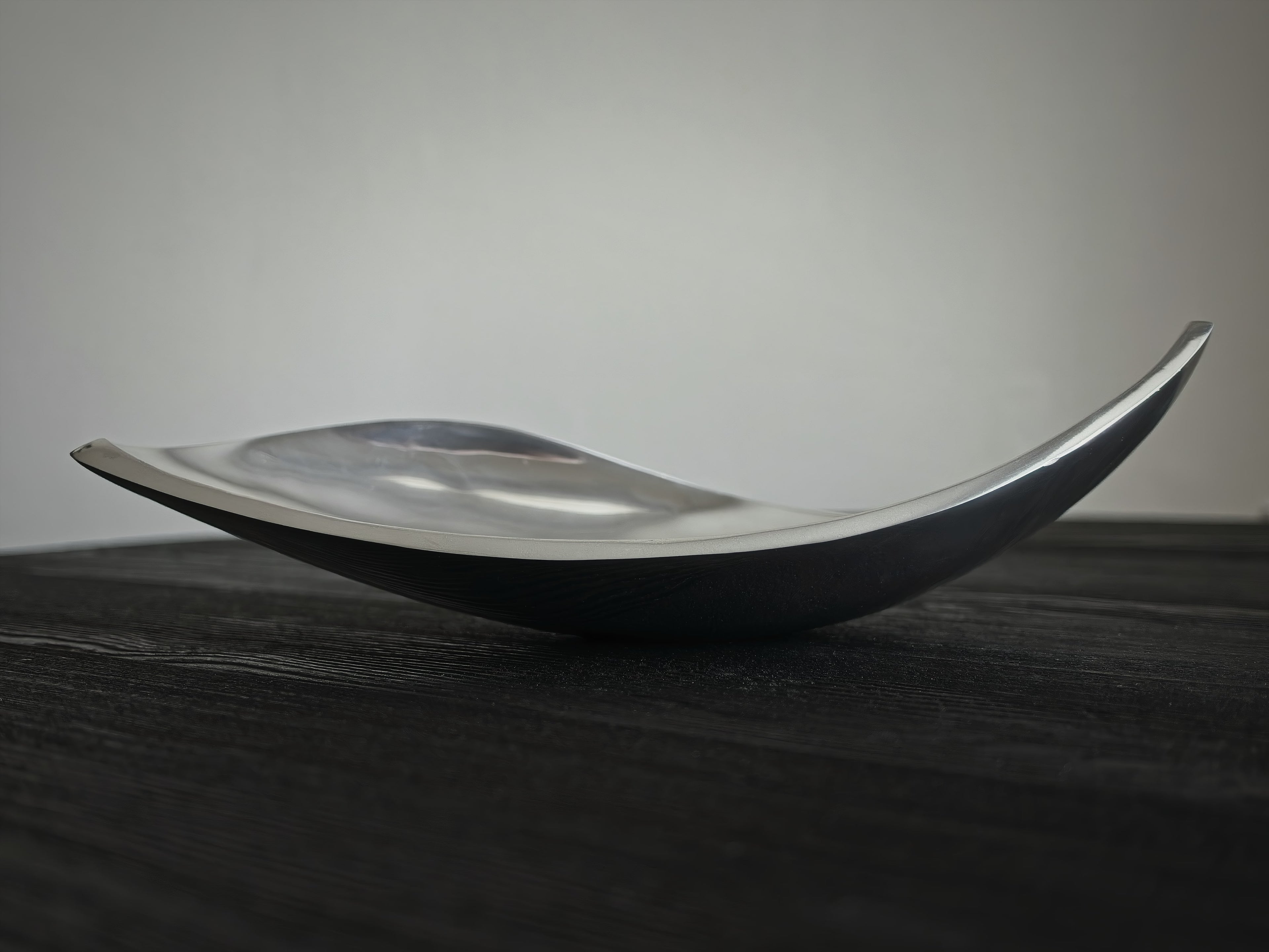 A mid century modern vintage sculptural silver home décor dish on a dark surface with a neutral background.