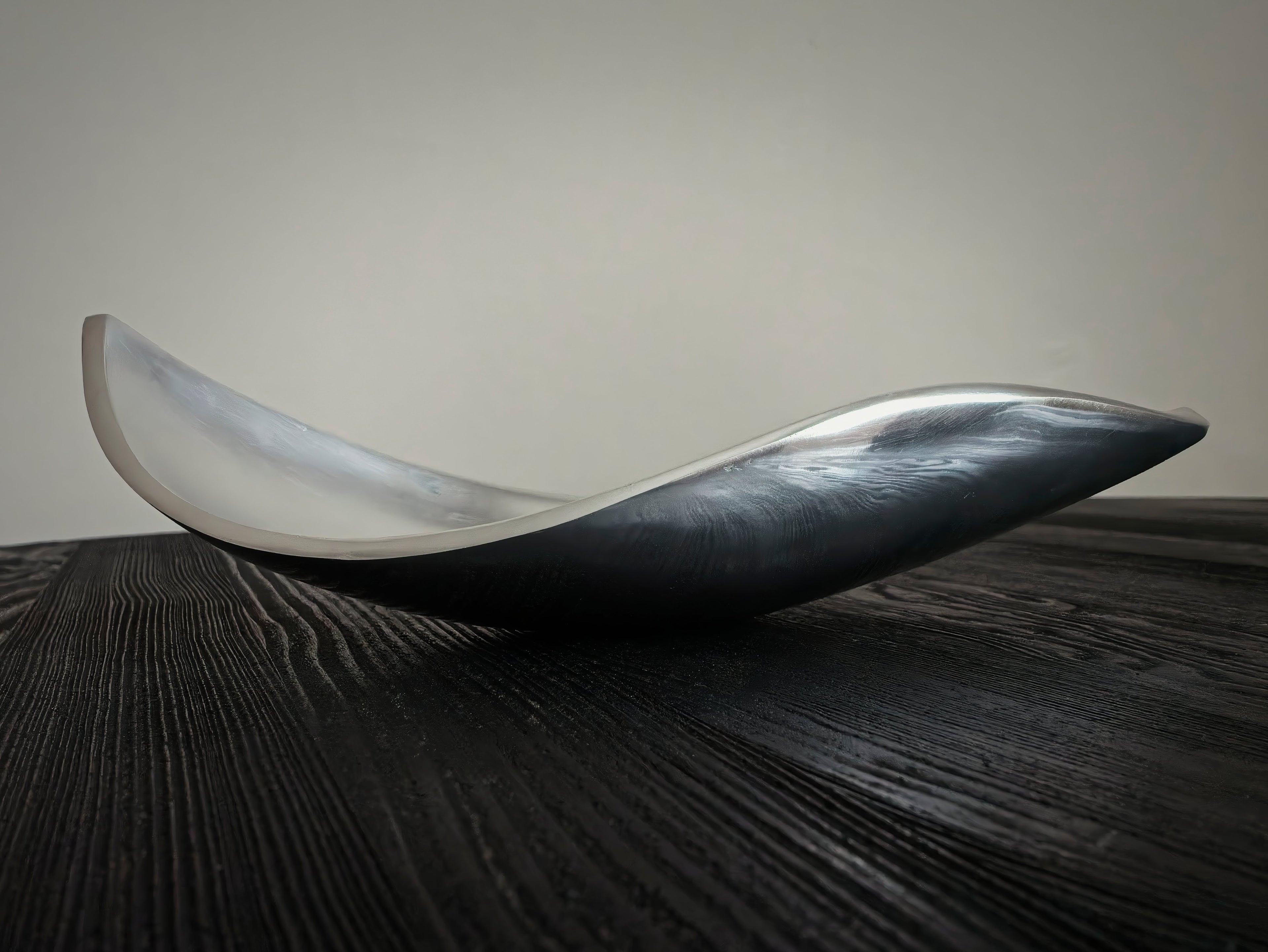 A 1980s mid century modern, curved stainless steel dish on a dark wooden surface with a neutral background.