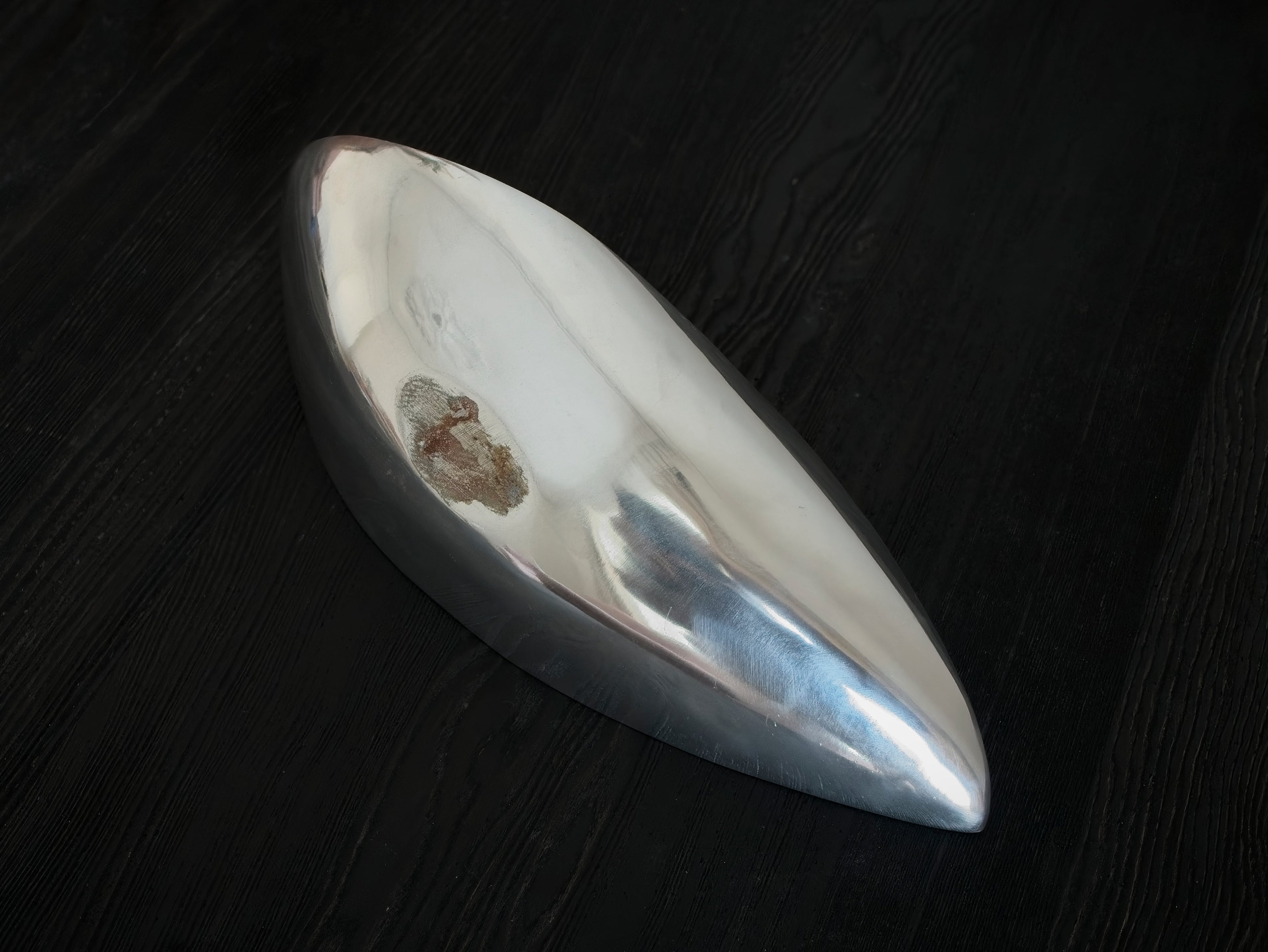 The bottom of a mid century modern vintage silver dish on a dark wooden surface.