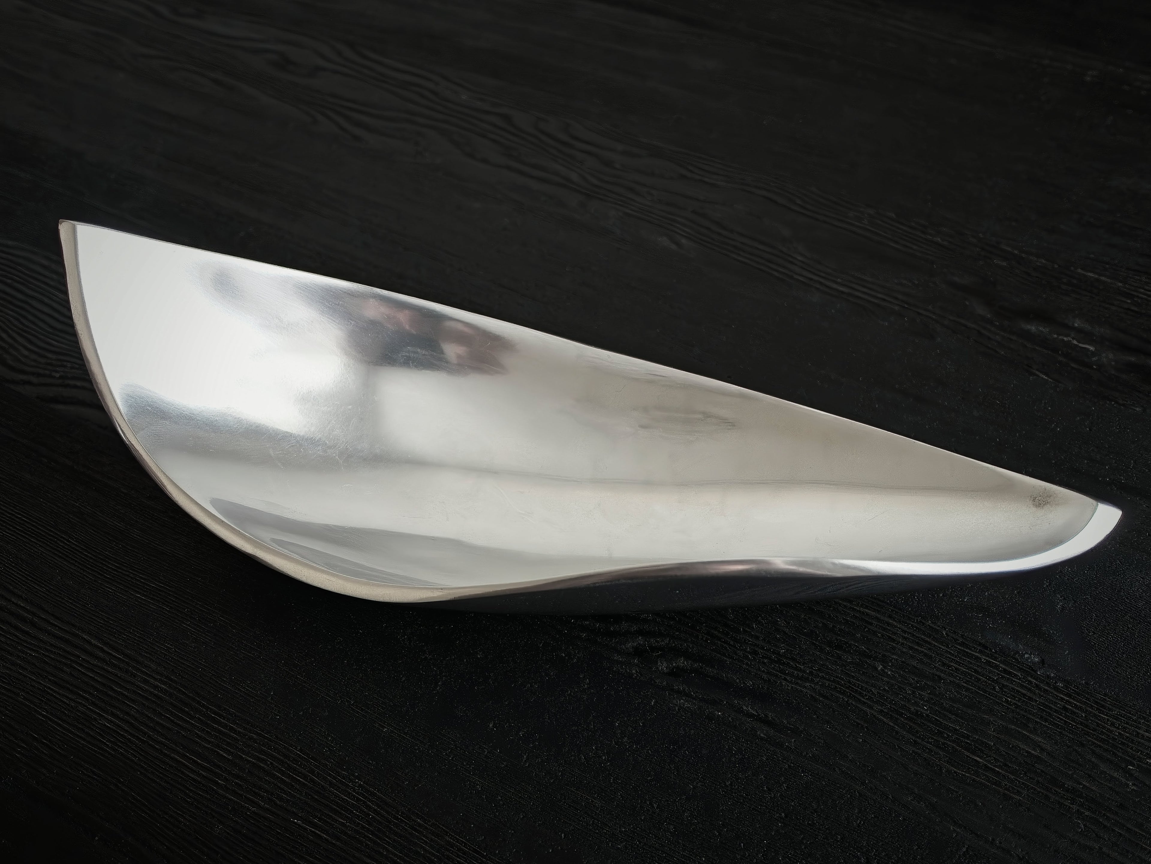 A space age mid century modern vintage silver dish with futuristic curved edges on a dark wooden surface from above.