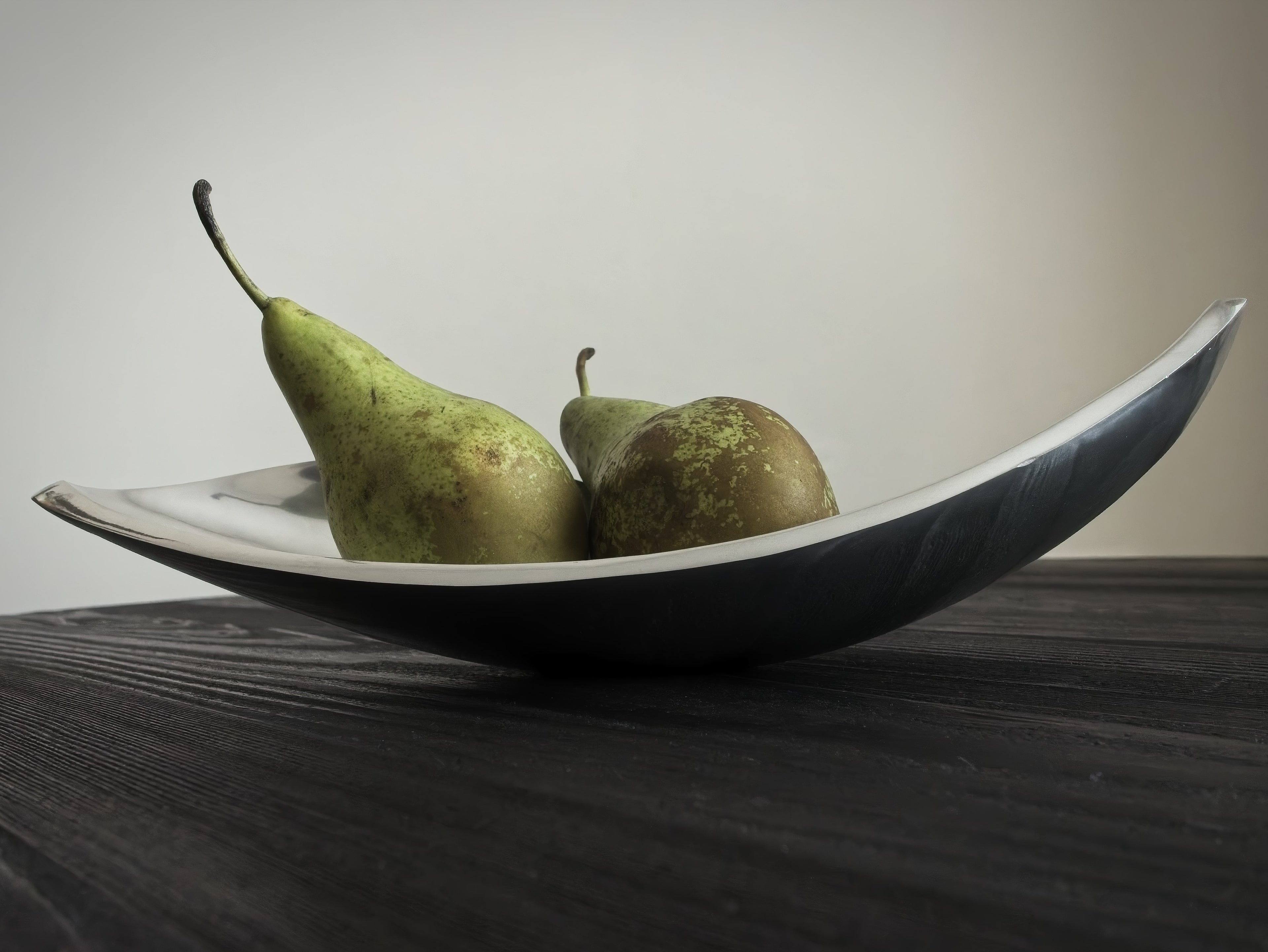 Two green pears in a black and white bowl on a wooden surface with a neutral background