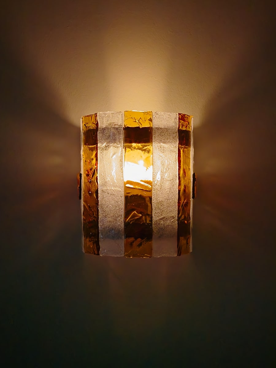 A unique vintage mid century modern wall lamp by Carlo Nason for Mazzega lit from within with a warm glowing light on a dark background.